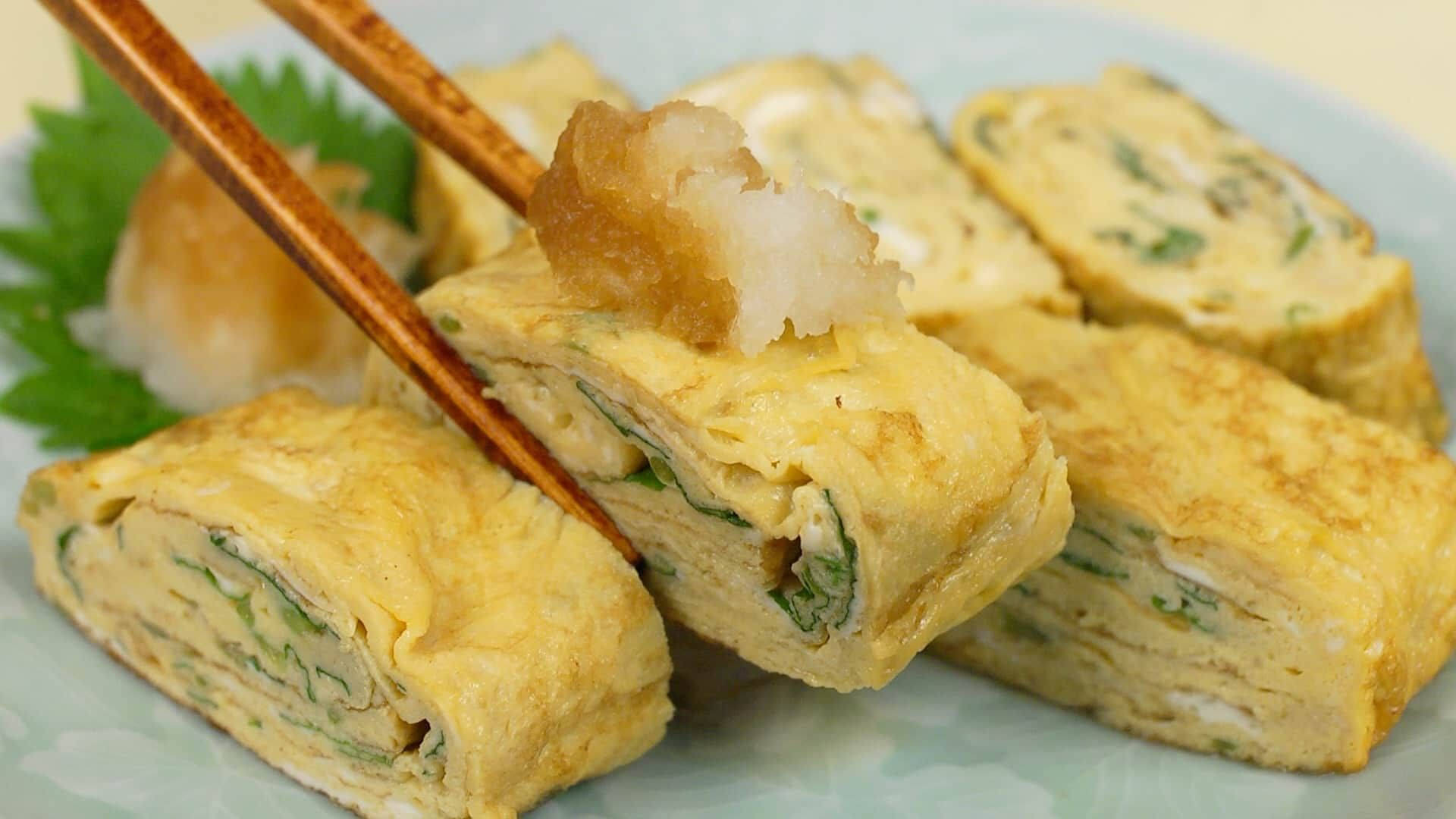Egg 桌布 壁紙 — 切片日式玉子燒蛋捲，配上青蔥和天婦羅配料，放在淺藍色盤子上，附有筷子。