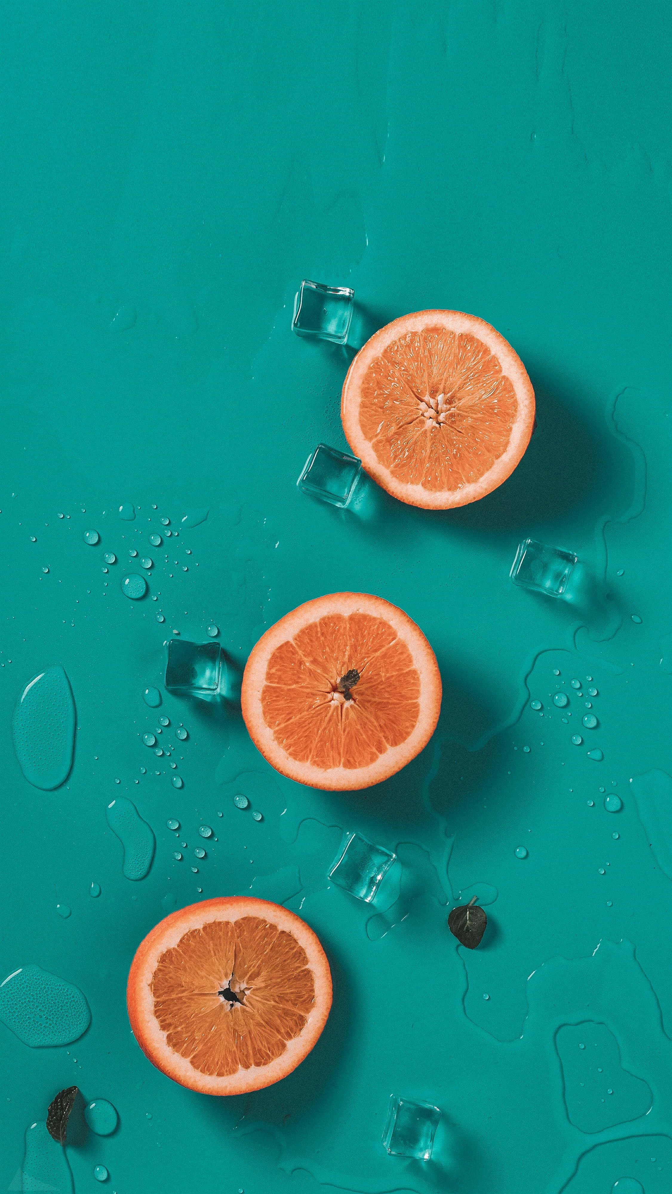 Orange And Teal 桌布 壁紙 — 切片柳橙和冰塊放在濕潤的青綠色表面上，周圍散落著水滴和深色種子。