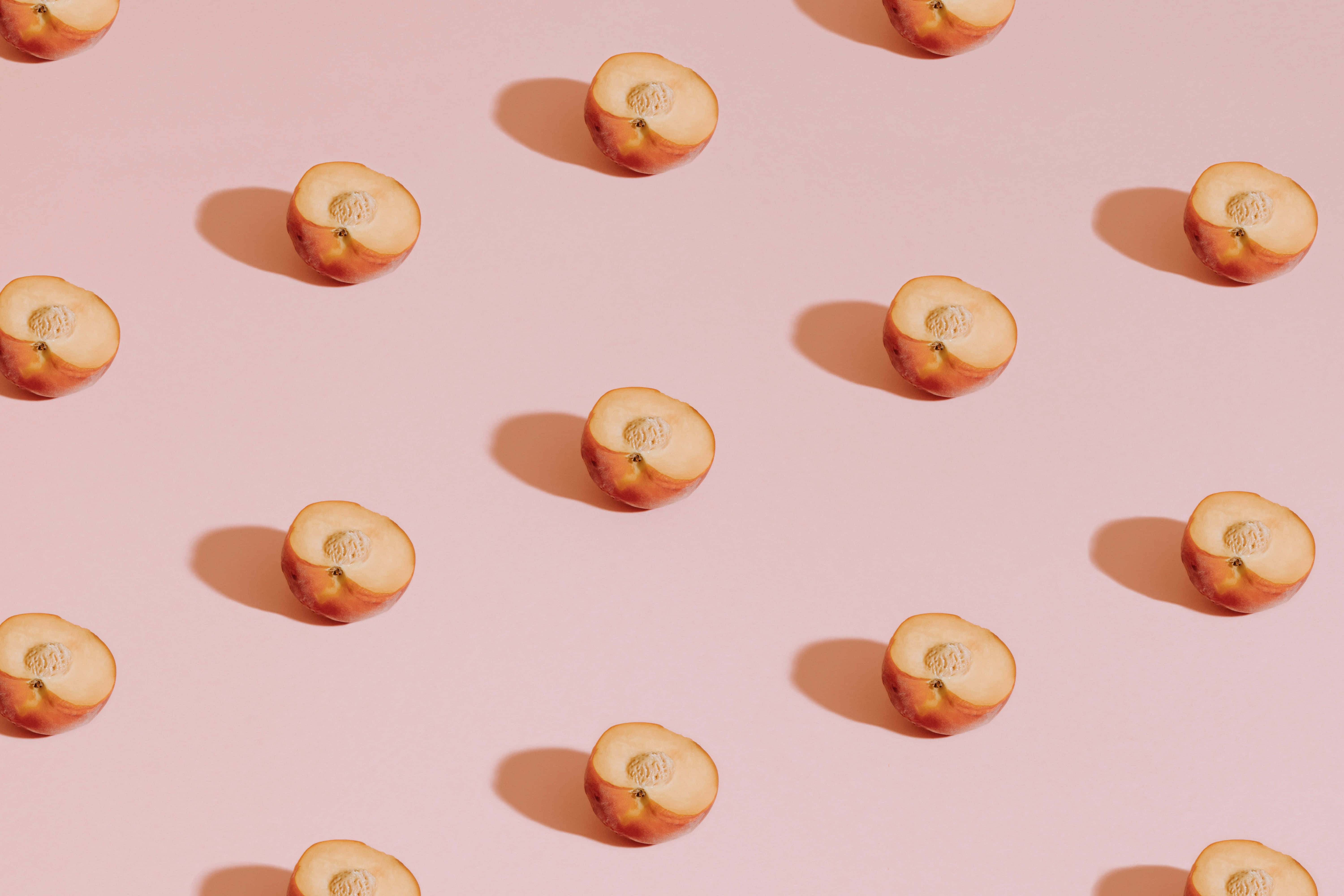 Peaches 桌布 壁紙 — 切片桃子在柔軟的粉紅色背景上以散落圖案排列，帶有柔和陰影。