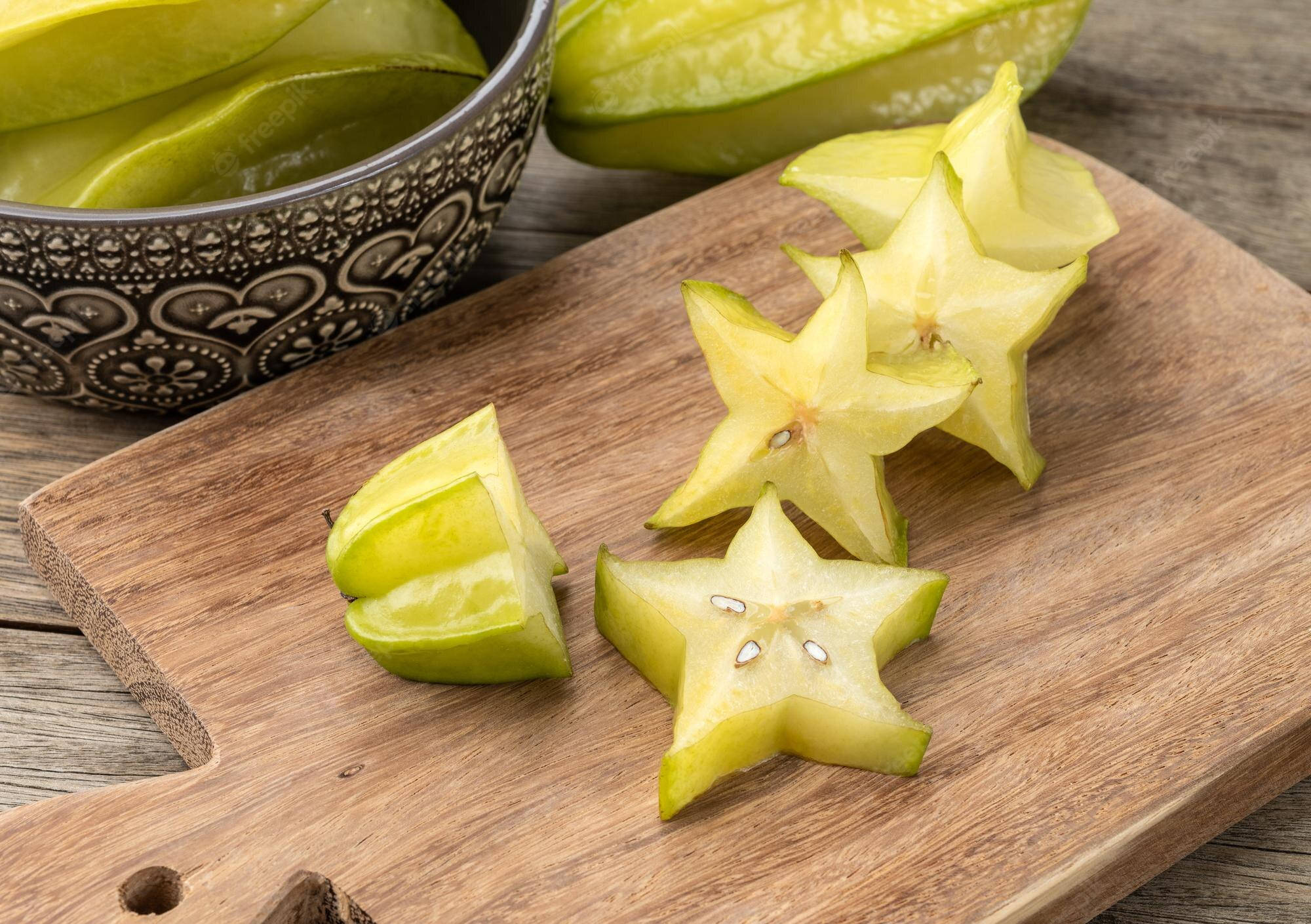 Fruits 桌布 壁紙 — 切片楊桃排列在木砧板上，背景有完整水果和圖案碗。