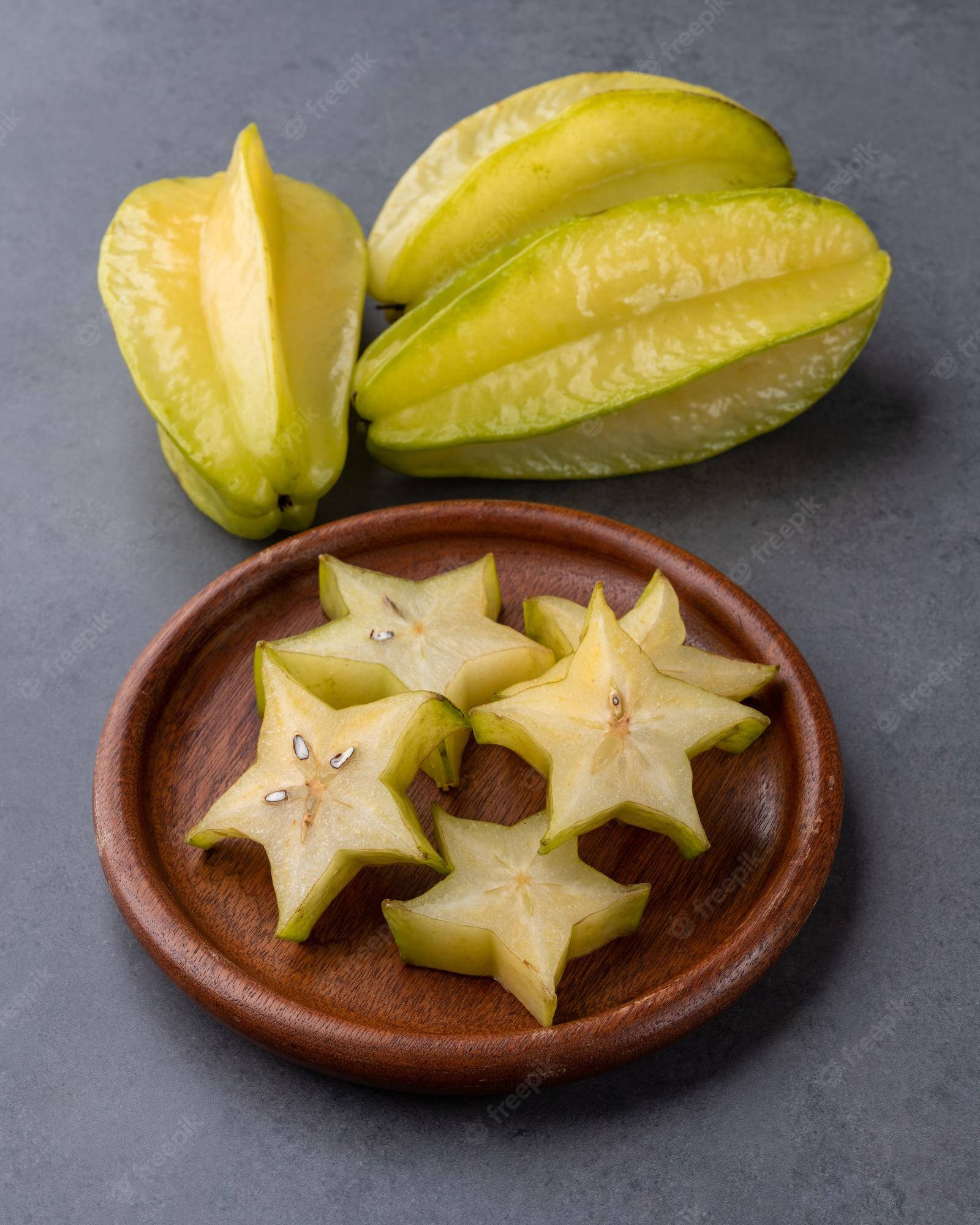 Fruits 桌布 壁紙 — 切片楊桃擺放在木盤上，旁邊有完整水果，置於灰色表面。