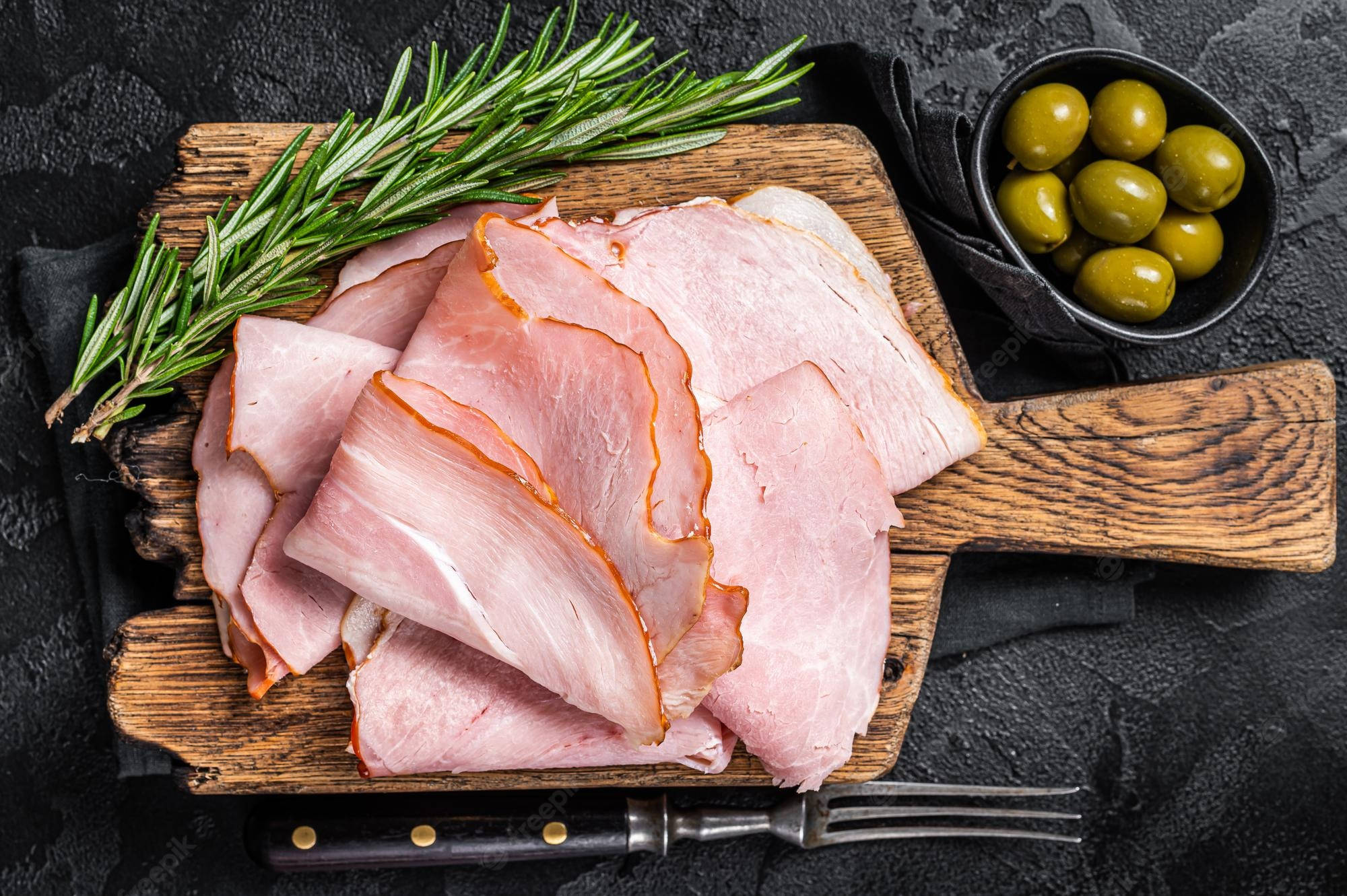 Ham 桌布 壁紙 — 切片火腿配迷迭香和青橄欖，擺放在質樸的木砧板上，背景為深色紋理。