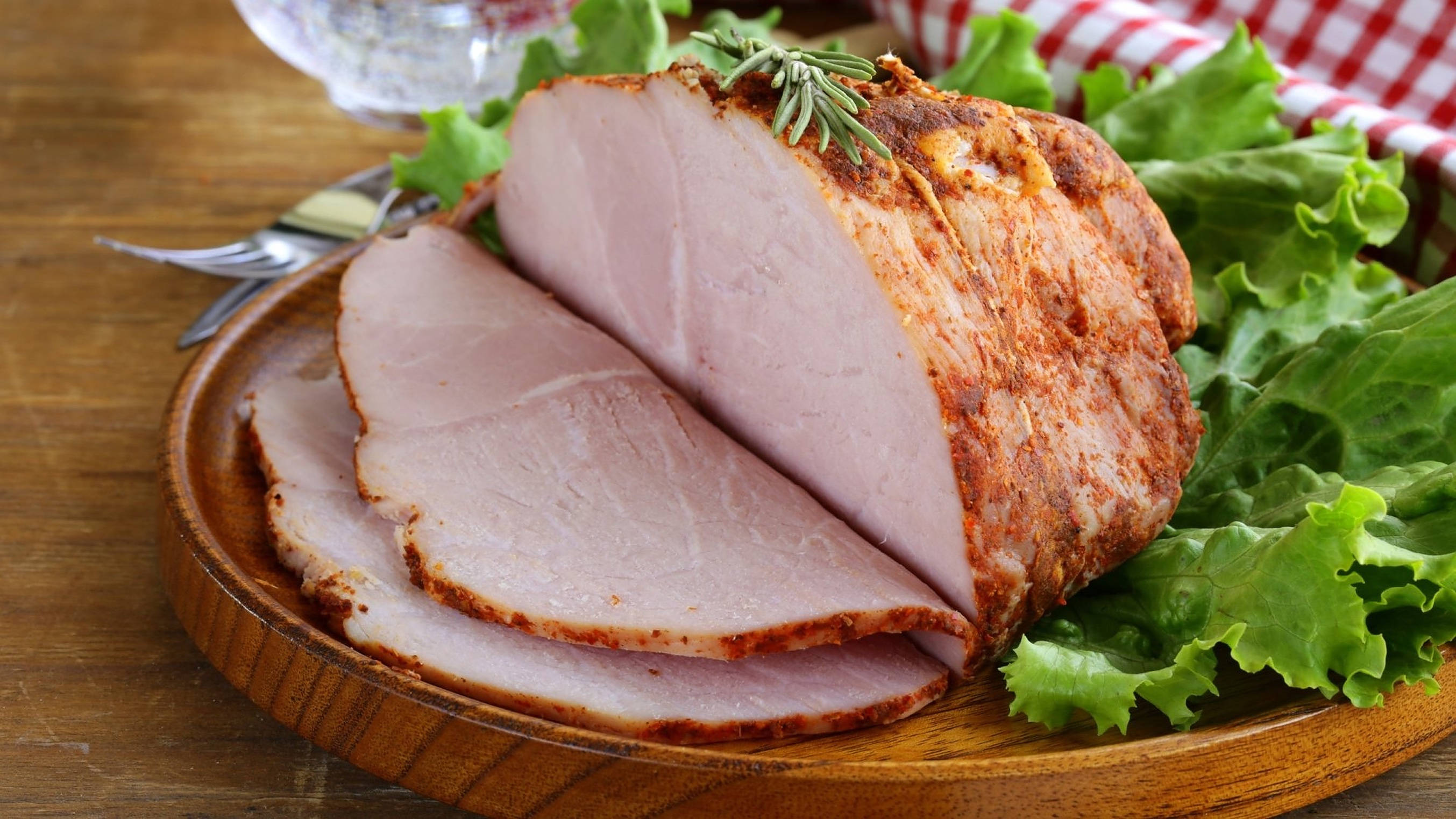 Ham 桌布 壁紙 — 切片烤火腿搭配迷迭香裝飾，置於木盤上，旁邊襯以爽脆的綠色生菜。