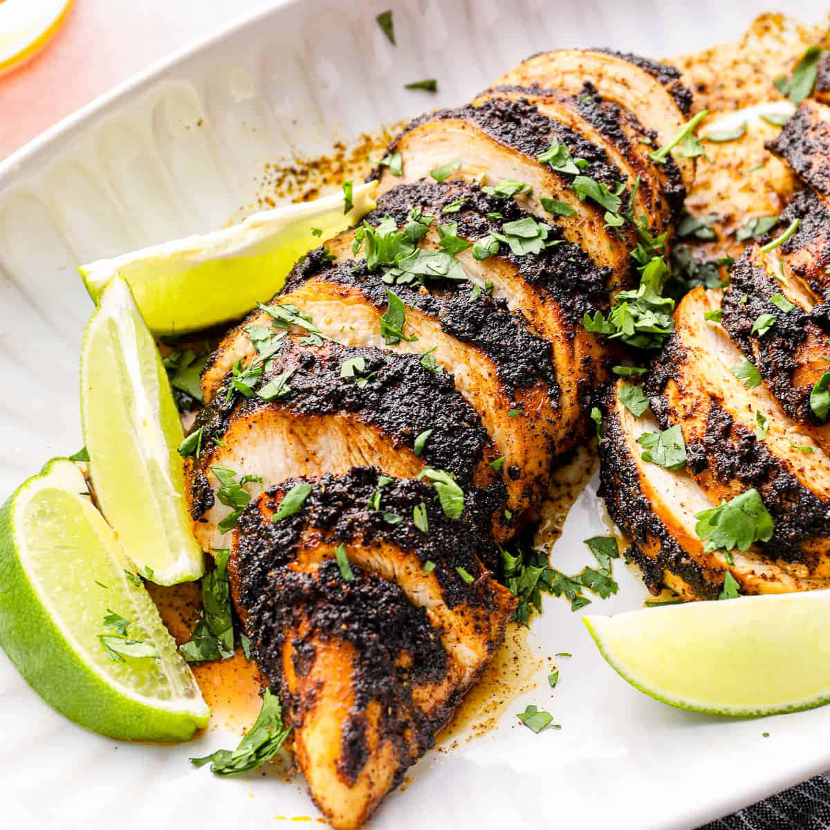 Blackened Chicken 桌布 壁紙 — 切片烤雞搭配深色香料抹醬和新鮮香菜，飾以萊姆角，盛於白盤上。
