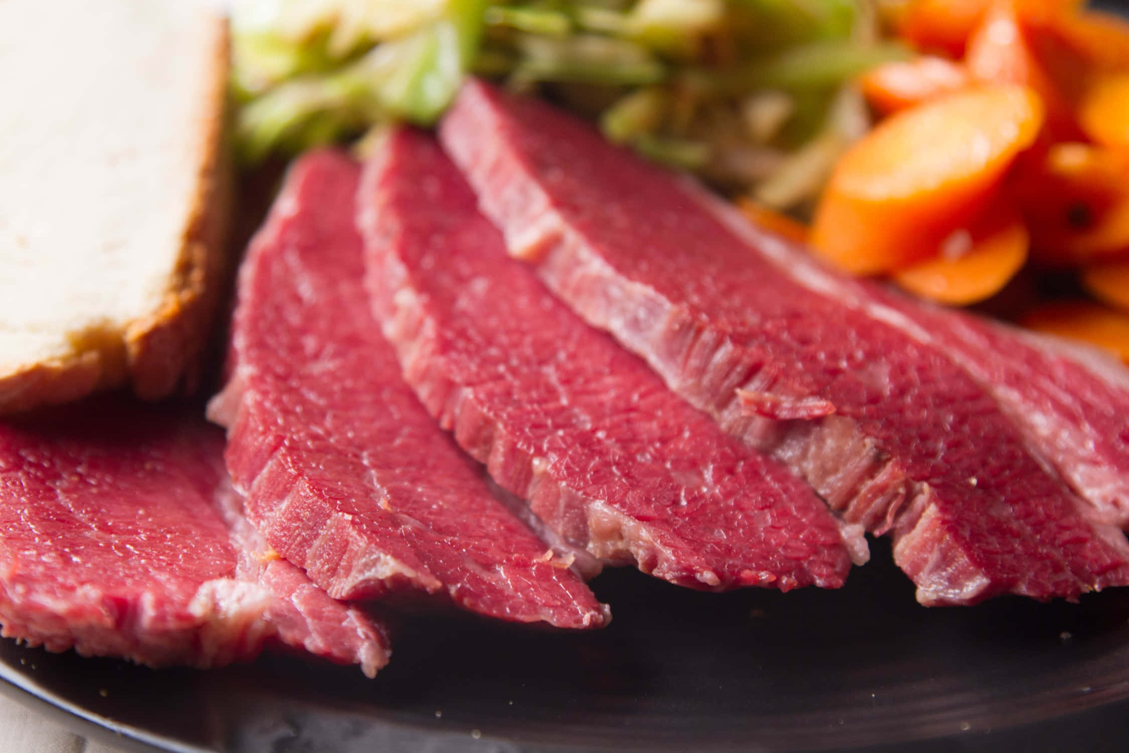 meat 桌布 壁紙 — 切片生烤牛肉配紅蘿蔔和青菜，放在深色盤子上，旁邊有麵包。