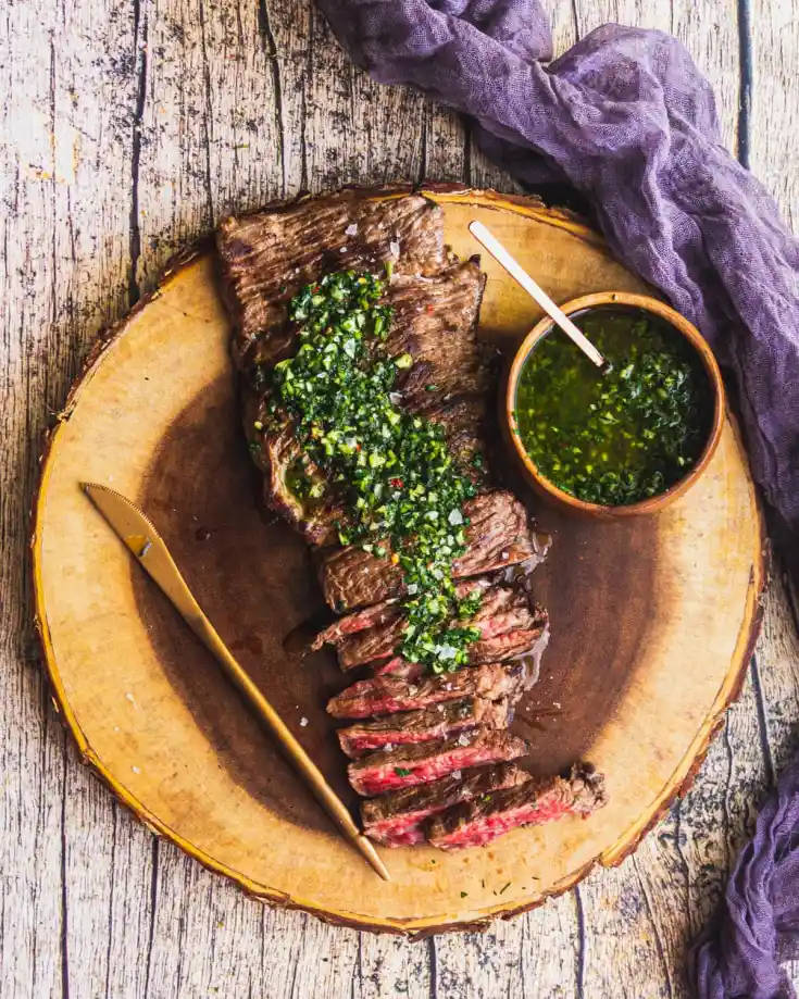 meat 桌布 壁紙 — 切片的中等熟度牛排，上面淋上新鮮的奇米丘里醬，放在一個鄉村風木盤上，旁邊有塊紫色布。