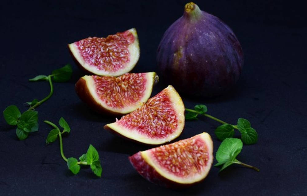 Food Photography 桌布 壁紙 — 切片紫色無花果，帶有粉紅色果肉和新鮮薄荷葉，排列在深色紋理表面上。