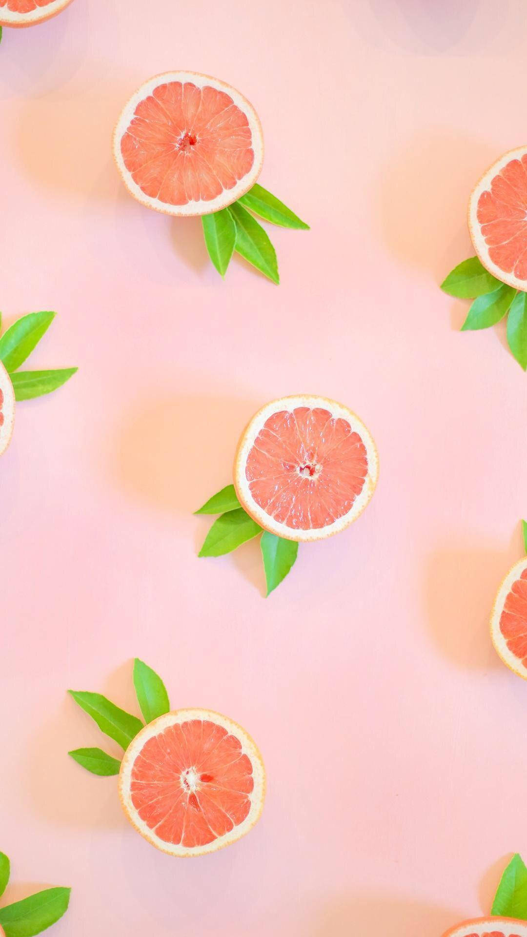Fruits 桌布 壁紙 — 切片葡萄柚搭配綠葉，在柔和粉紅色背景上以平鋪方式排列。