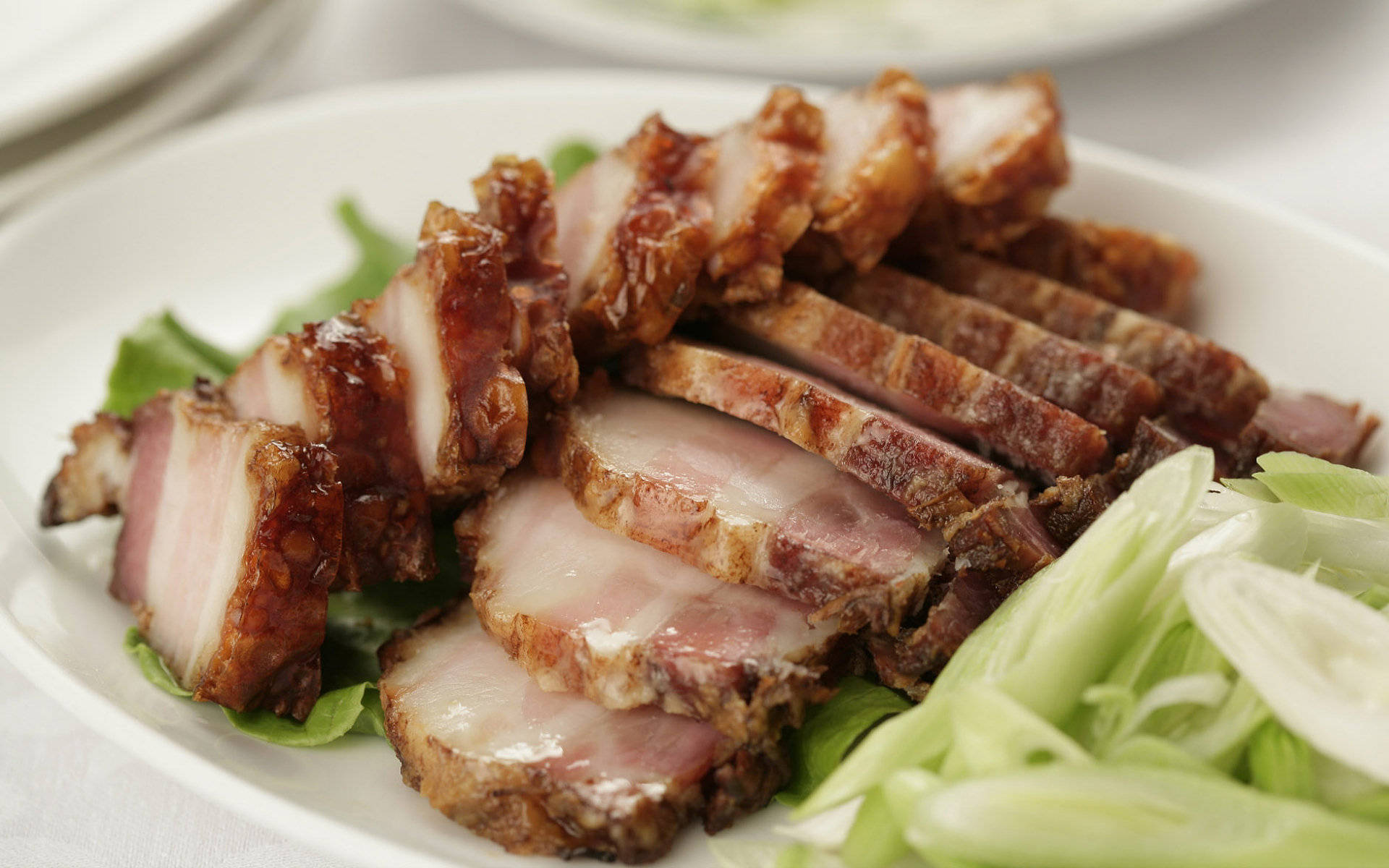 4K Food 桌布 壁紙 — 切片蜜汁烤豬肉，邊緣酥脆，內裡多汁，盛載於白色盤子上，搭配新鮮生菜和青蔥。