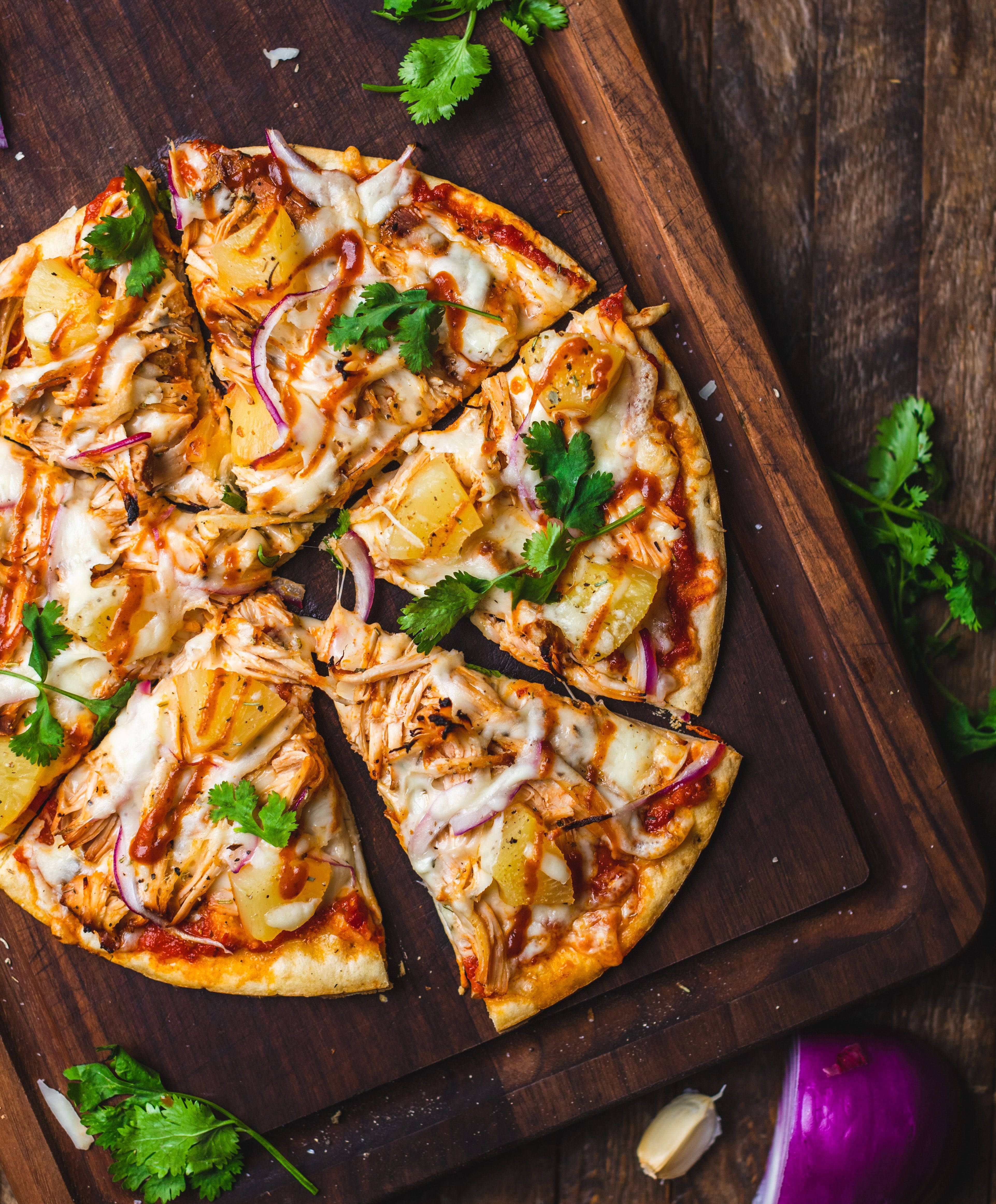Dominos Pizza 桌布 壁紙 — 切片雞肉披薩配上鳳梨、紅洋蔥和香菜，放在深色木砧板上。