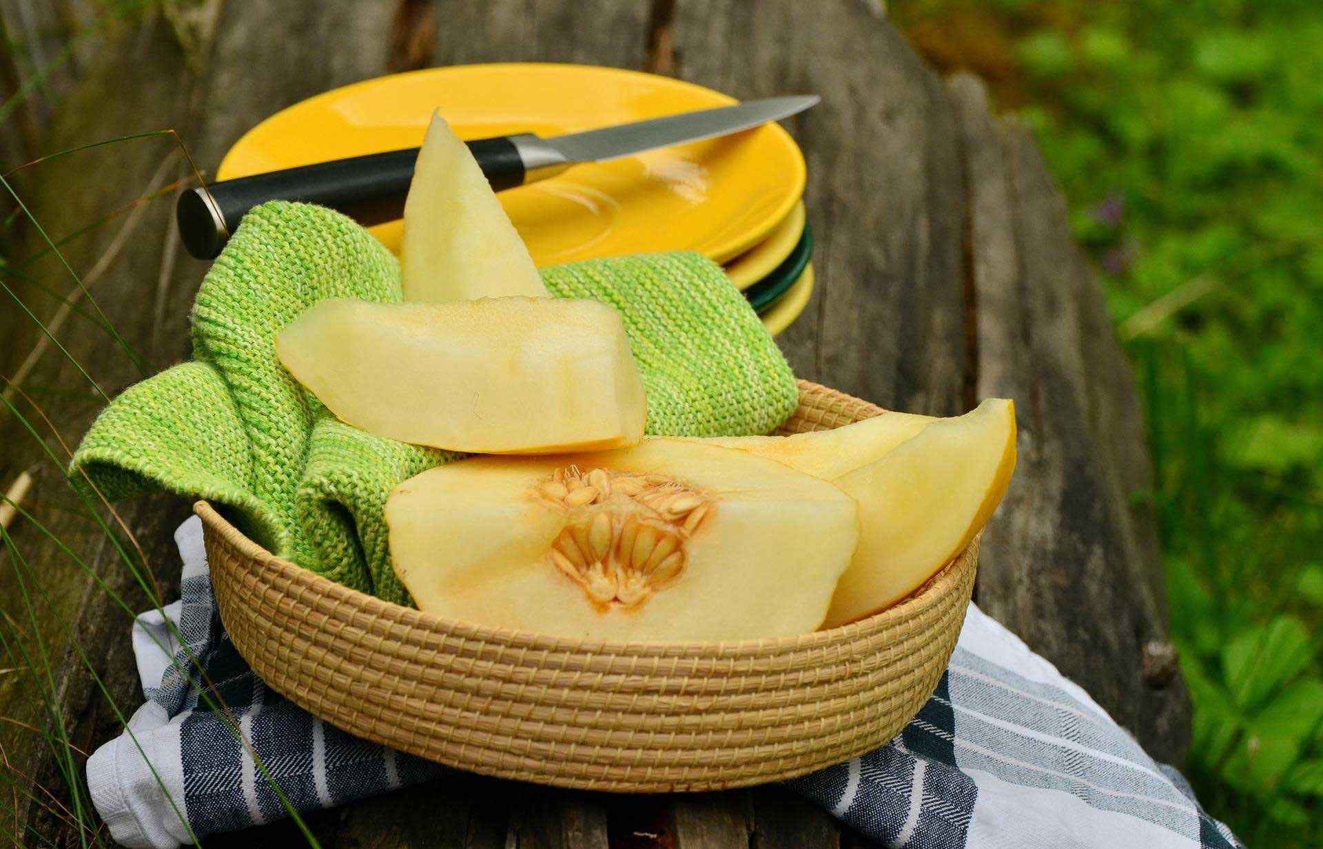 Fruits 桌布 壁紙 — 切片黃色蜜瓜放在木桌上的編織籃中，桌上有綠色布和黃色盤子。