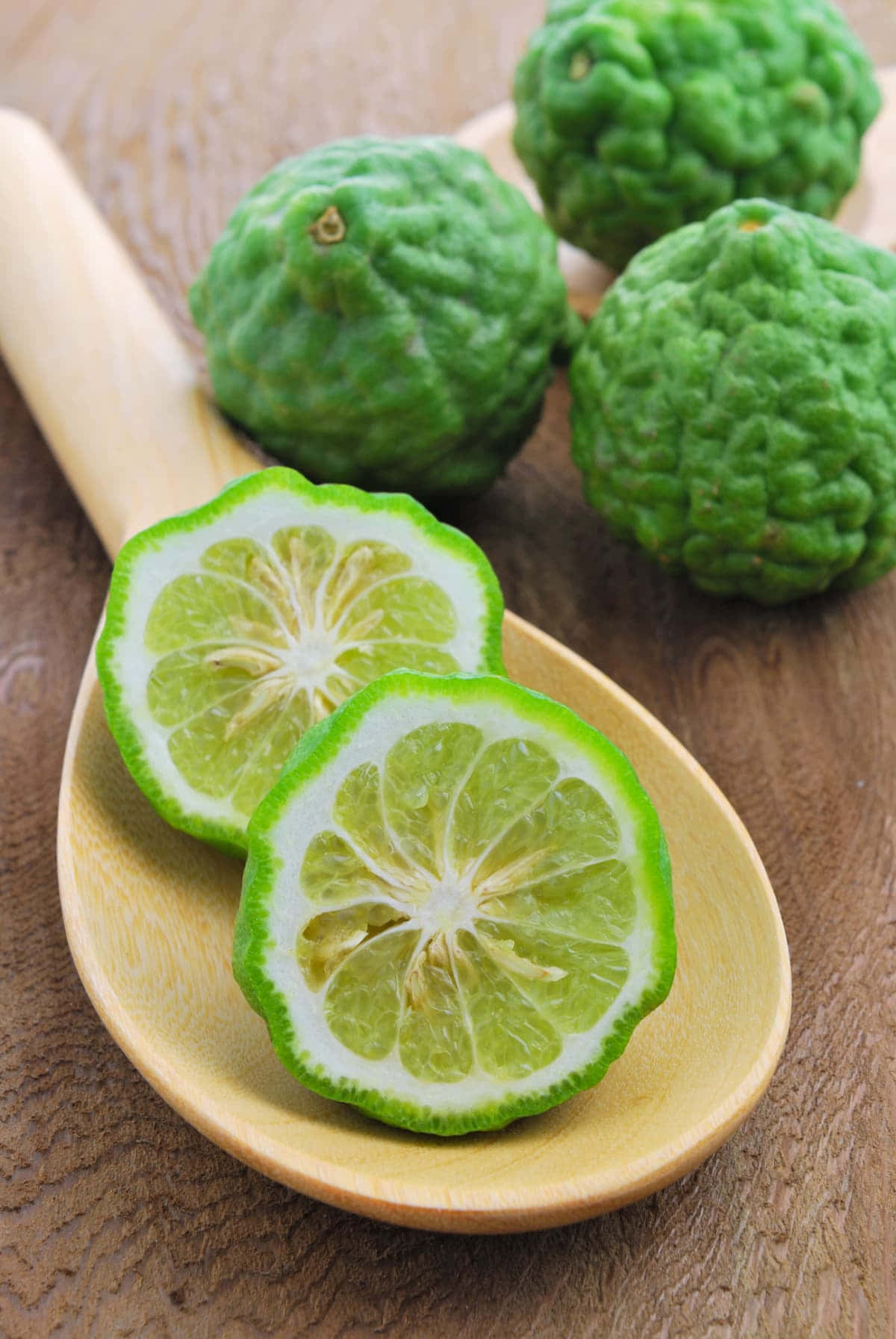 Fruit 桌布 壁紙 — 切開的綠色萊姆，表皮凹凸不平，放在木湯匙上，旁邊有完整的萊姆，一起在鄉村風格的木桌面上。