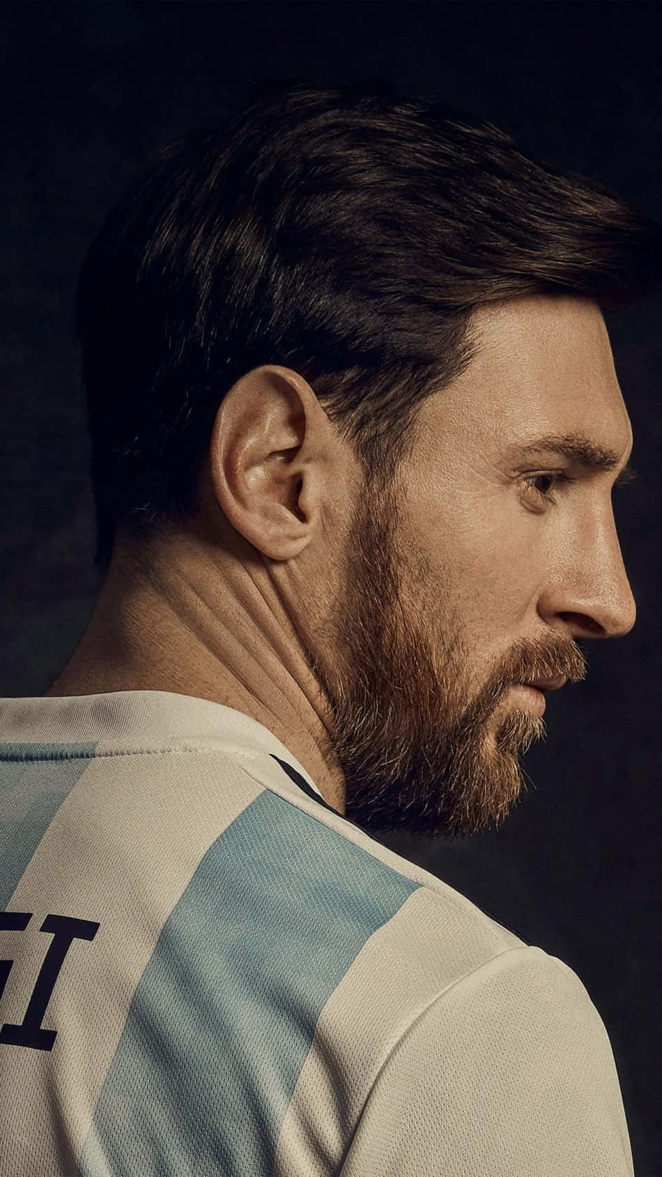 Messi Cool 桌布 壁紙 — 利昂內爾·梅西身穿阿根廷球衣的近距離肖像，在深色背景下若有所思地越過肩膀凝視。