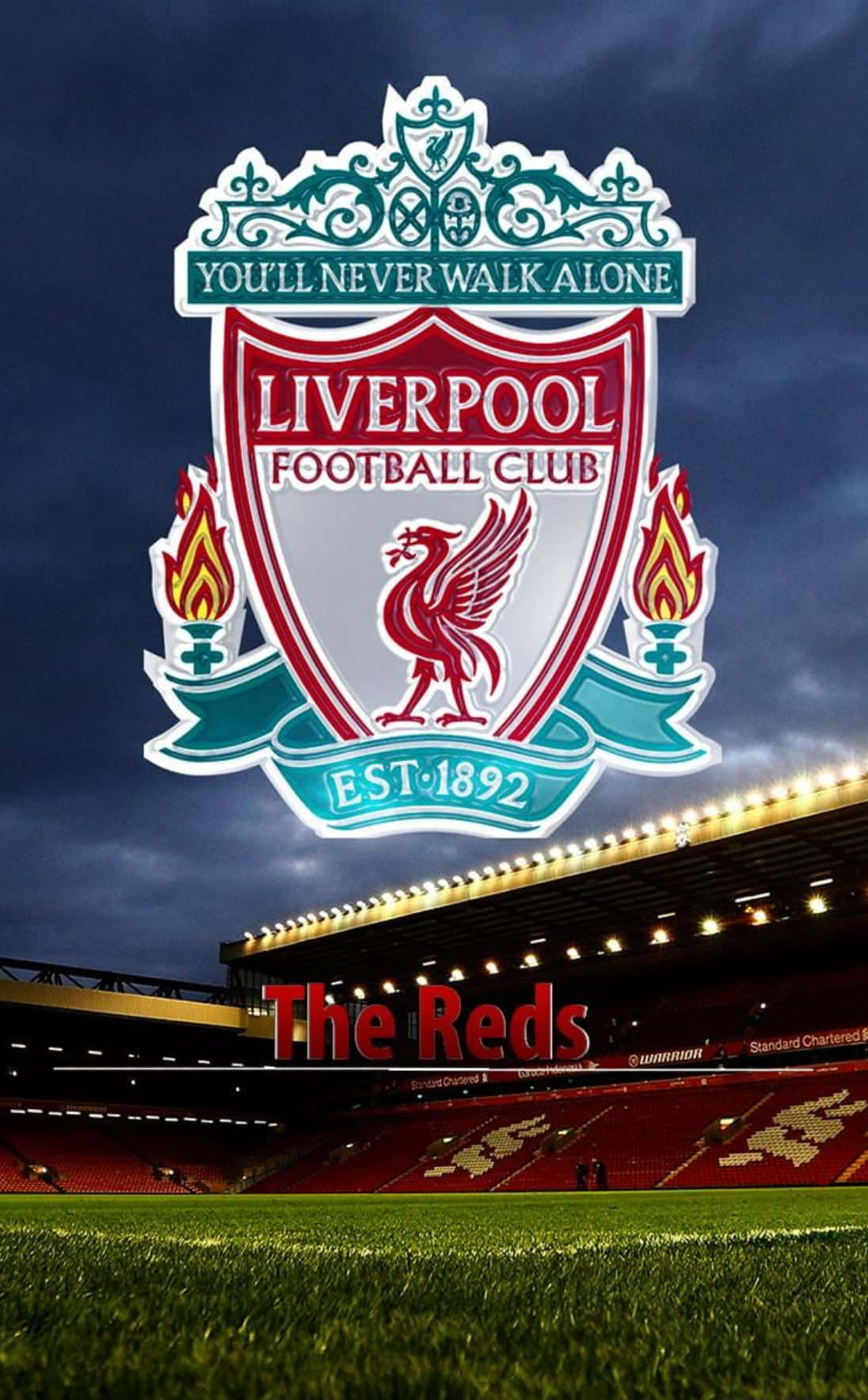 Liverpool Logo 桌布 壁紙 — 利物浦足球俱樂部徽章在黑暗天空下，於安菲爾德球場上方發光，下方是鮮紅色的座位和綠色草坪。