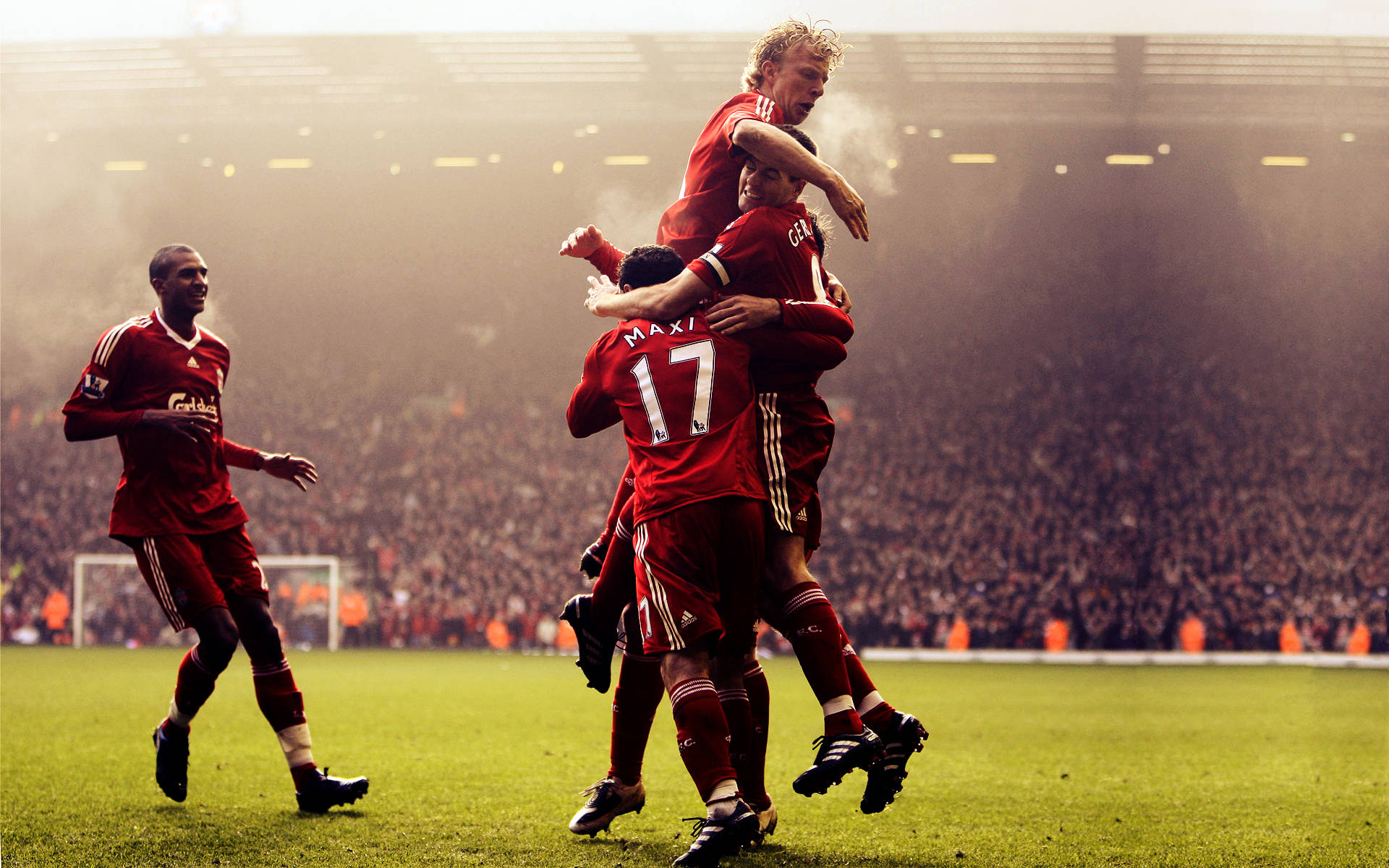Liverpool Fc 桌布 壁紙 — 利物浦足球員身穿紅色球衣，在陽光明媚的球場上以喜悅的擁抱慶祝進球。