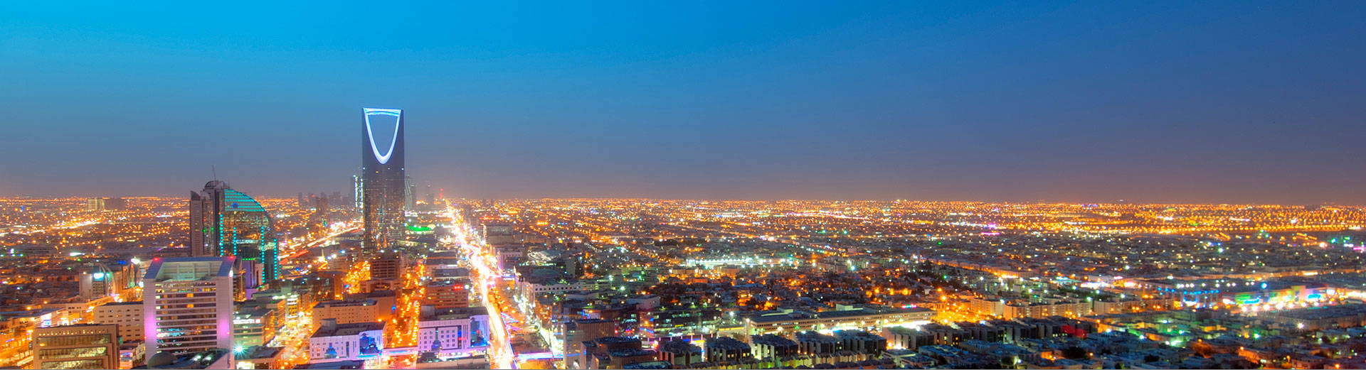 Riyadh 桌布 壁紙 — 利雅德城市景觀的 panoramic 夜景，街道閃爍，標誌性塔樓在深藍色天空下。