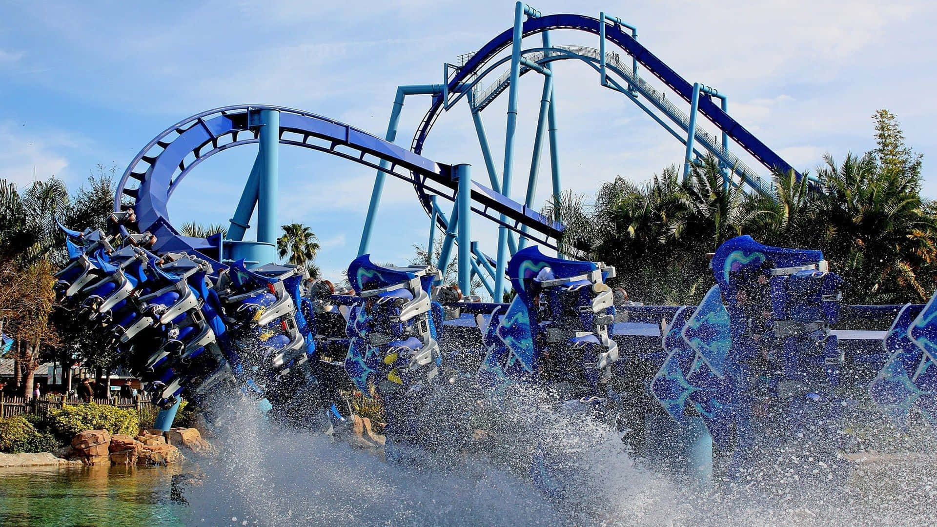 Roller Coaster 桌布 壁紙 — 刺激的藍色水上雲霄飛車在晴朗天空下彎過泳池，將乘客拋入水花之中。