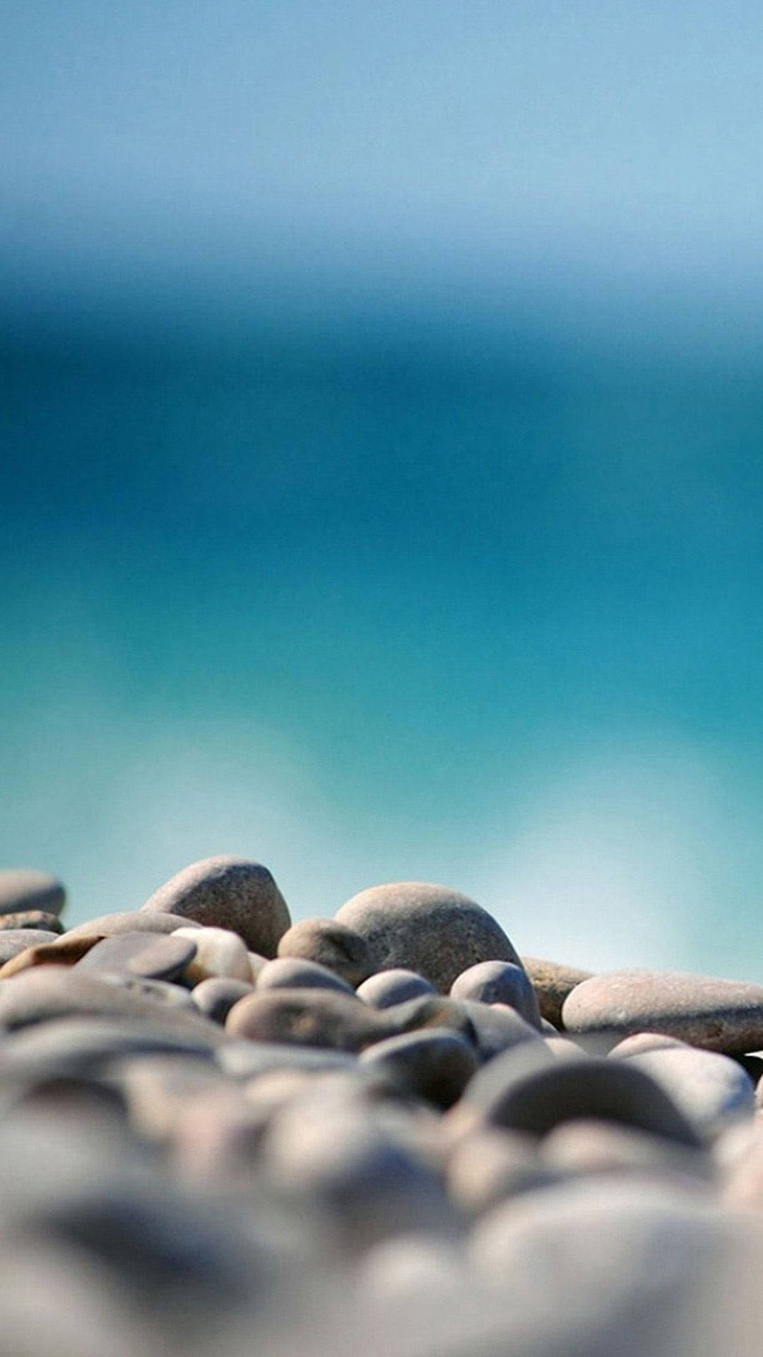 Stone 桌布 壁紙 — 前景光滑圓潤的鵝卵石在清澈藍天下模糊融入碧綠海洋。
