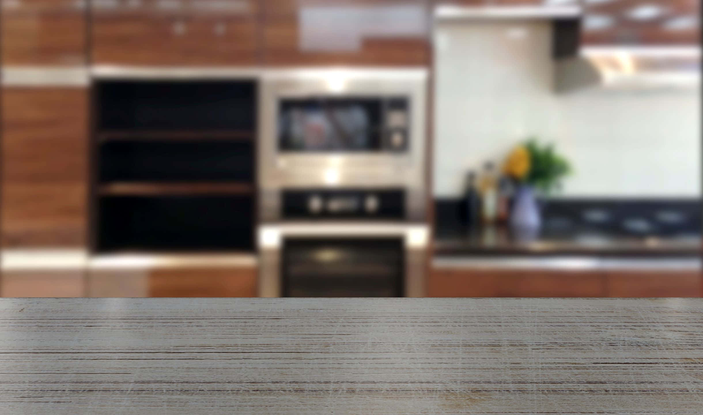 kitchen 桌布 壁紙 — 前景是一張樸實的木桌面，背景是模糊的現代廚房，有不鏽鋼電器和溫暖的木櫥櫃。