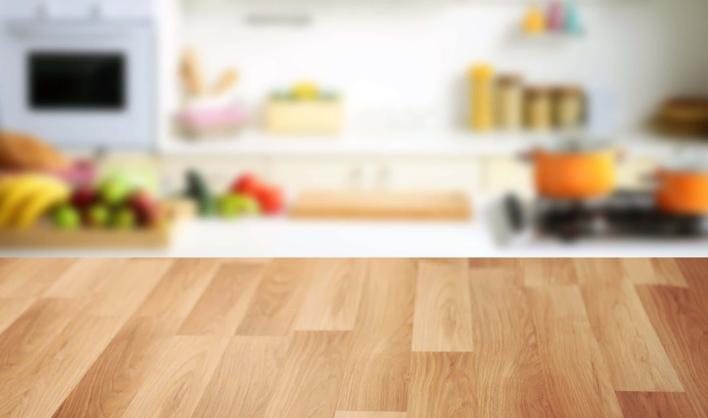 kitchen 桌布 壁紙 — 前景溫暖的木地板，背景是柔和模糊的廚房，展示色彩繽紛的農產品和電器。