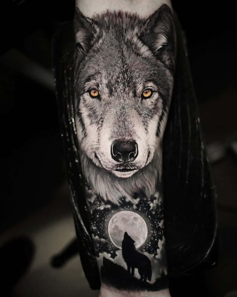 Beautiful Wolf 桌布 壁紙 — 前臂上一個超寫實的狼紋身，帶有發光的琥珀色眼睛和下方月光下嚎叫的狼場景。