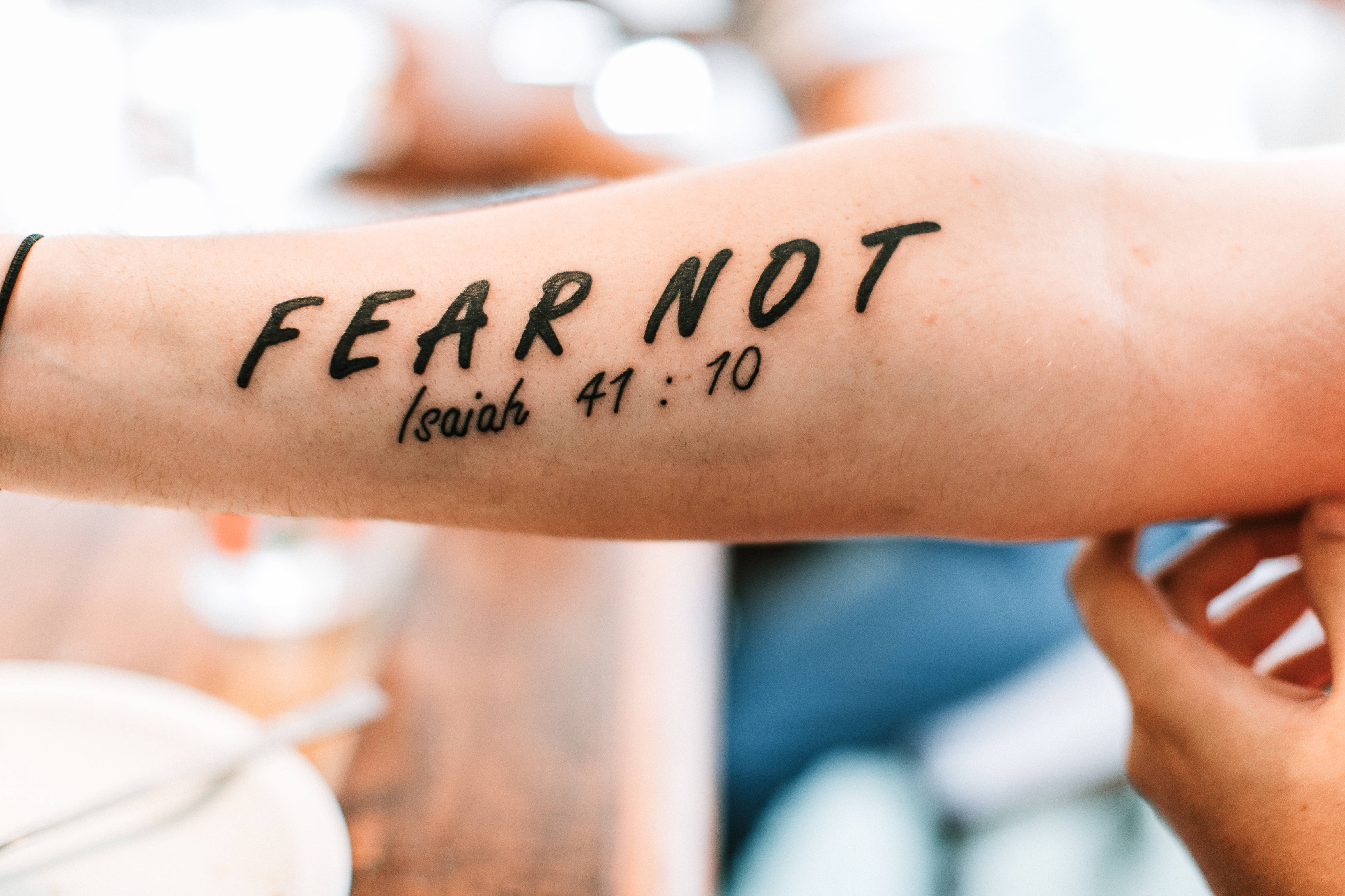 聖經經文 桌布 壁紙 — 前臂紋身特寫，上面用粗體黑色字體寫著「FEAR NOT 以賽亞書 41:10」，背景柔和模糊。