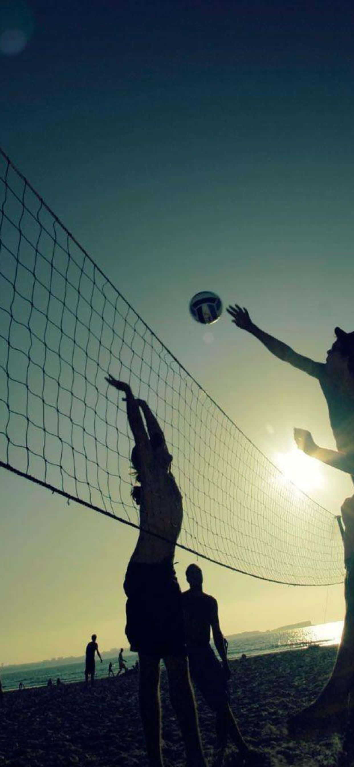 iPhone Xs Max Volleyball 桌布 壁紙 — 剪影中的沙灘排球選手跳起扣球，背景是發光的日落天空。