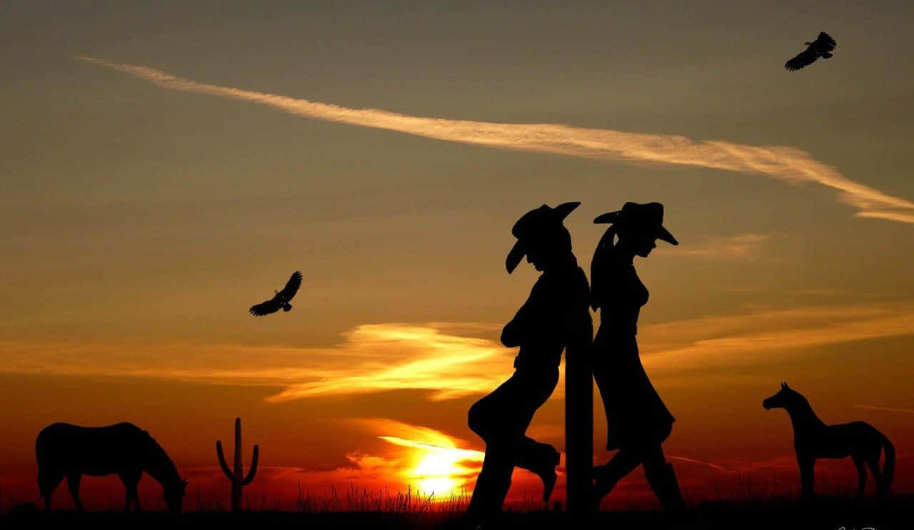 Desert 桌布 壁紙 — 剪影中的牛仔和女牛仔倚靠在柱子上，馬匹在吃草，鳥兒在火紅的日落天空中翱翔。