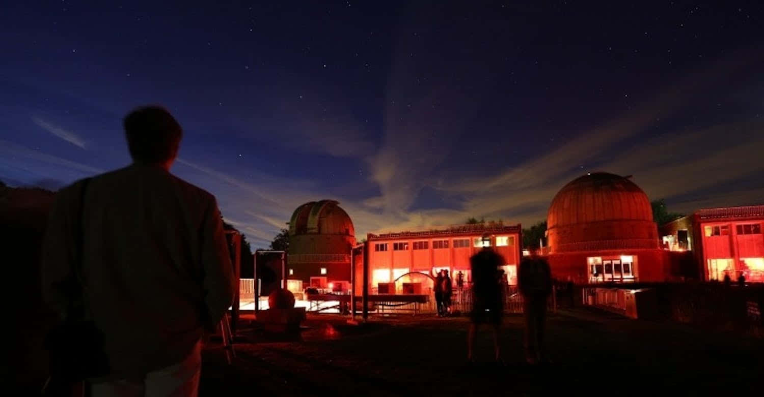 Observatory 桌布 壁紙 — 剪影人物凝視著溫暖燈光照耀下的天文台圓頂和建築上方的星空。