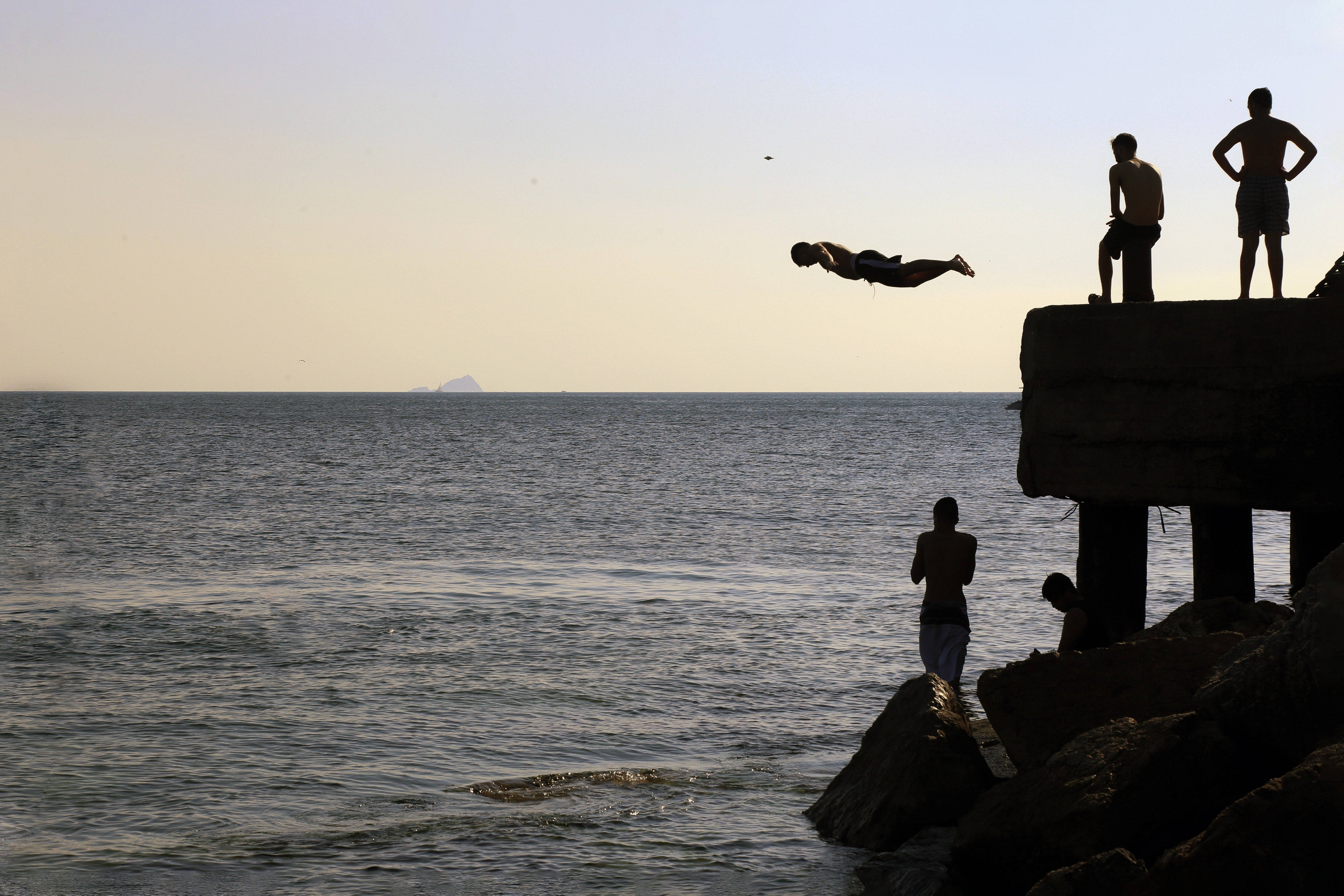 Jumping 桌布 壁紙 — 剪影人物在岩石碼頭上跳躍和站立，夕陽在平靜的海面上落下。