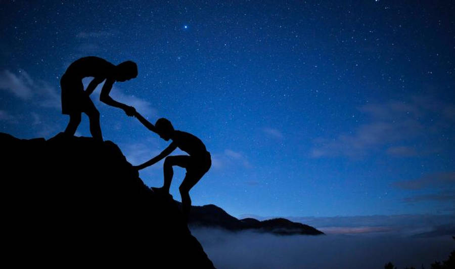 Friendship 桌布 壁紙 — 剪影人物在星空夜空中互相幫助攀登山峰，下方有雲層。
