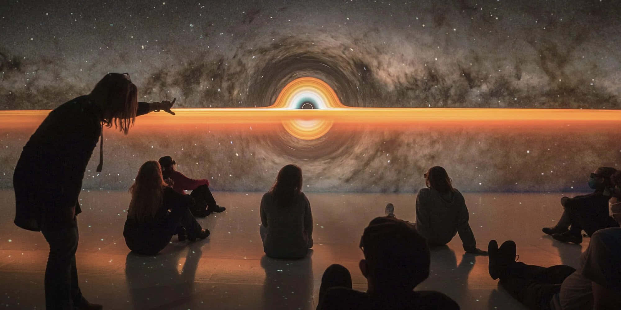 Deep 桌布 壁紙 — 剪影人物坐著並指向一個在星空宇宙展覽中巨大發光的黑洞投影。