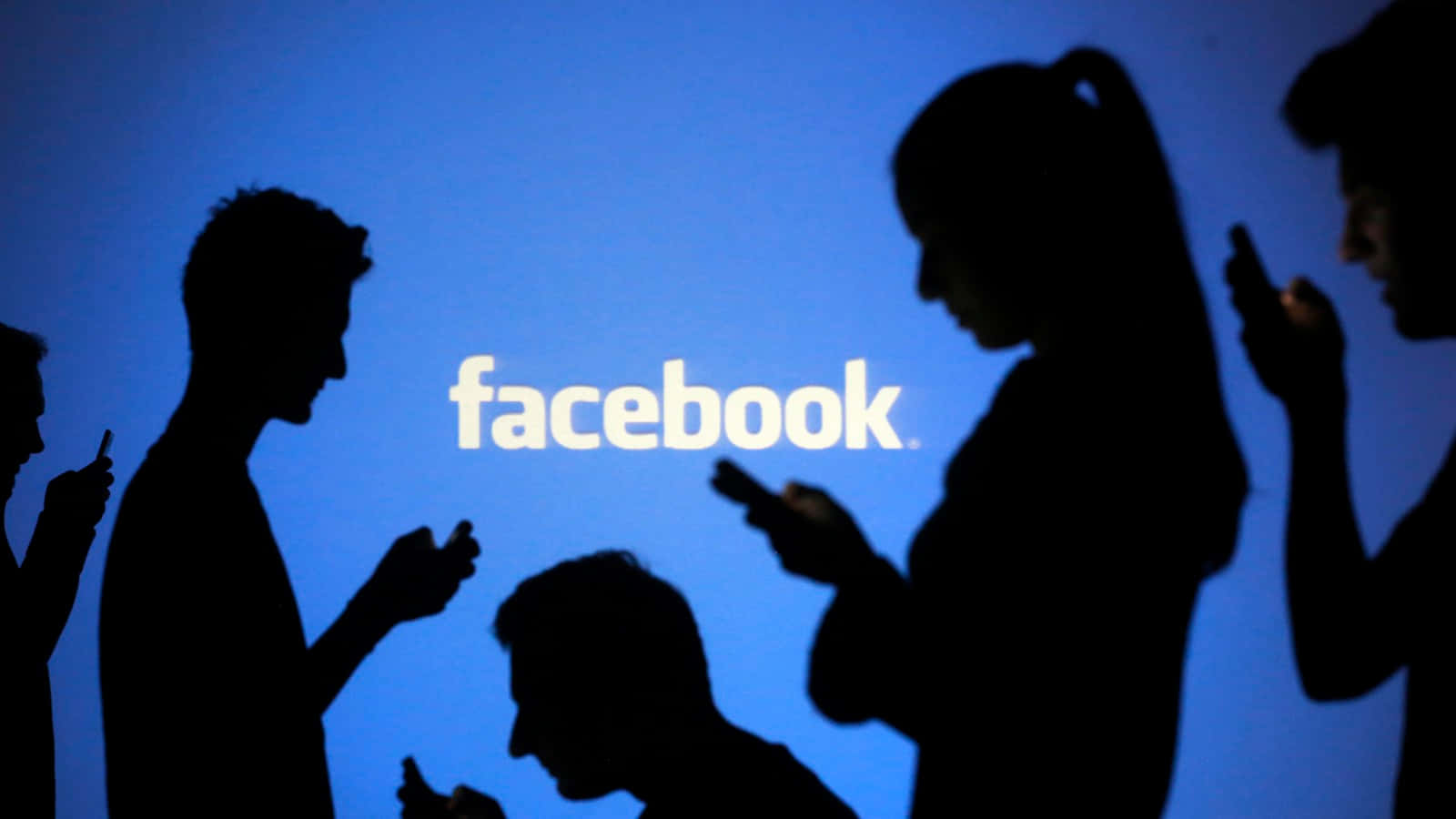 Facebook 桌布 壁紙 — 剪影人物專注於手機，背景是發光的藍色 Facebook 標誌。