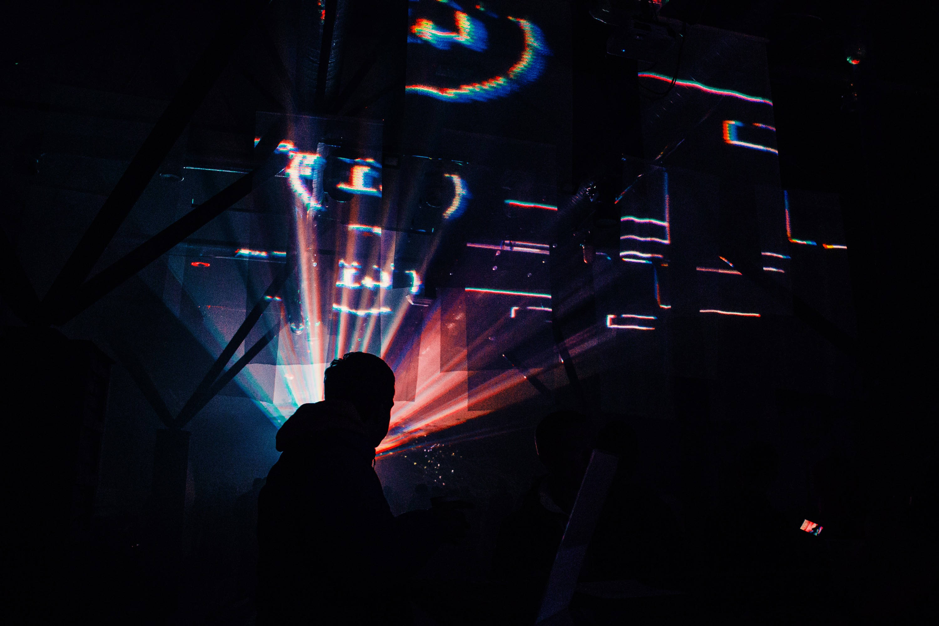 Party 桌布 壁紙 — 剪影人物觀看充滿活力的數位光投影在未來派俱樂部的黑暗幾何牆上舞動。