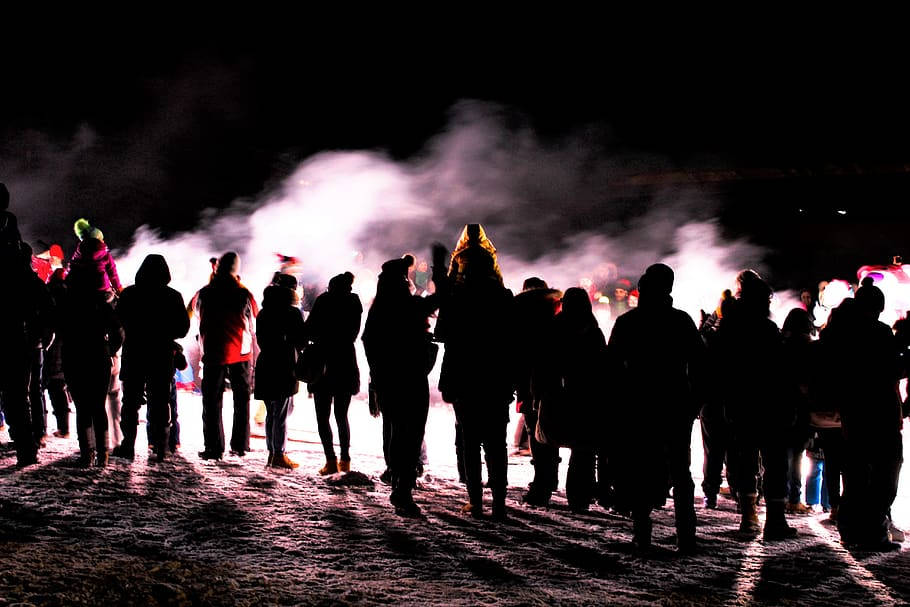 人物 桌布 壁紙 — 剪影人群在夜間站在雪地中，被明亮的發光燈光和上升的蒸汽照亮。