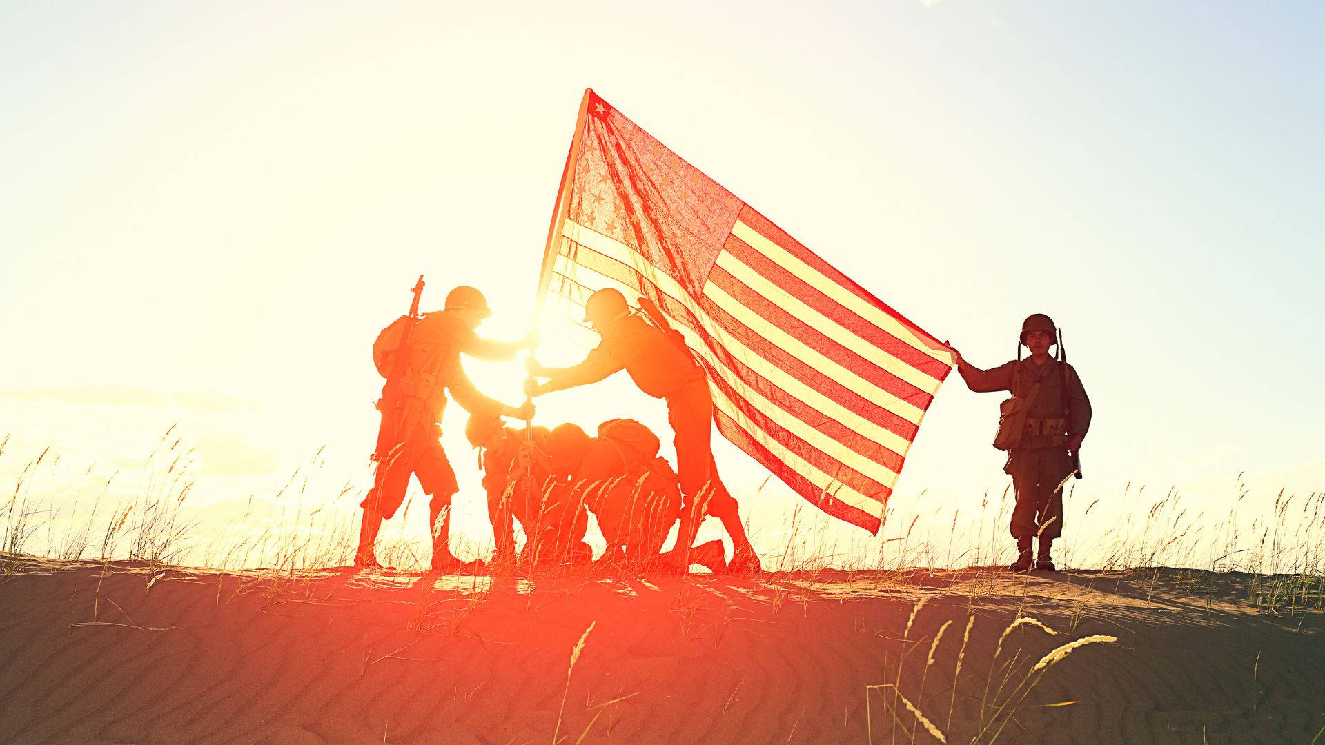 Military 桌布 壁紙 — 剪影士兵在金色日出時於沙丘頂升起美國國旗，前景草叢搖曳。