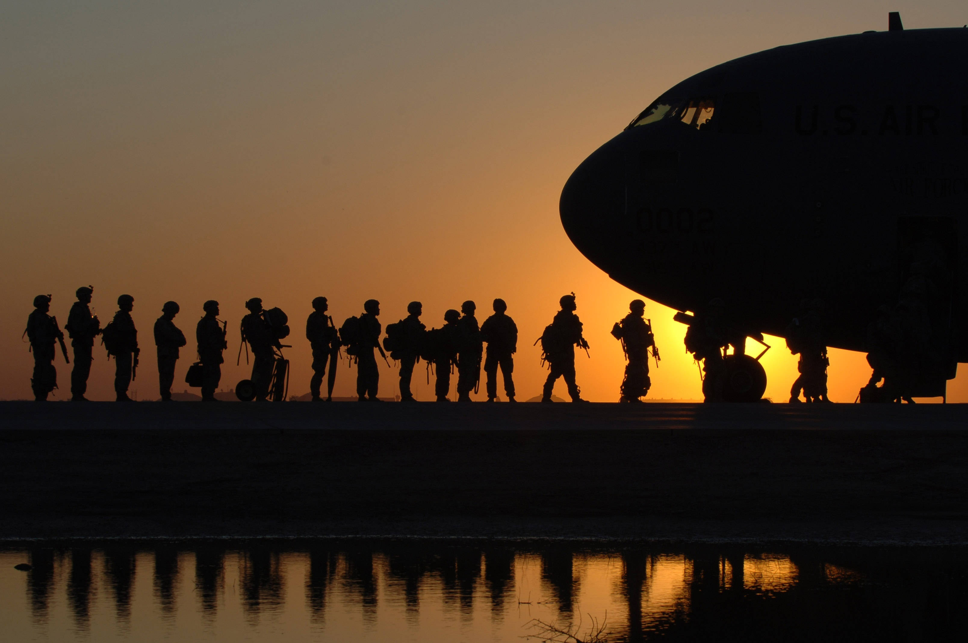 軍隊 桌布 壁紙 — 剪影士兵排隊站在大型軍用飛機旁邊，夕陽在他們身後落下，將溫暖的光線和倒影投射在下面的水面上。