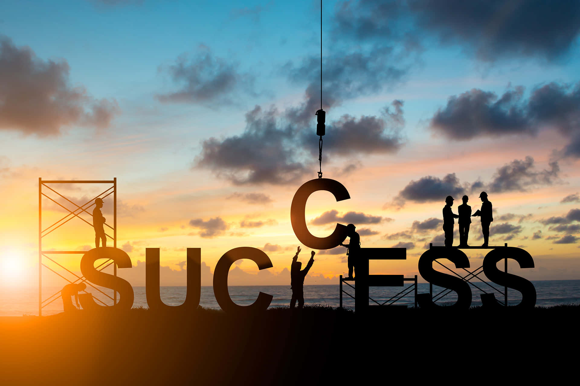 Success 桌布 壁紙 — 剪影工人在海洋上 vibrant 的日落背景下組裝一個巨大的 'SUCCESS' 標誌。