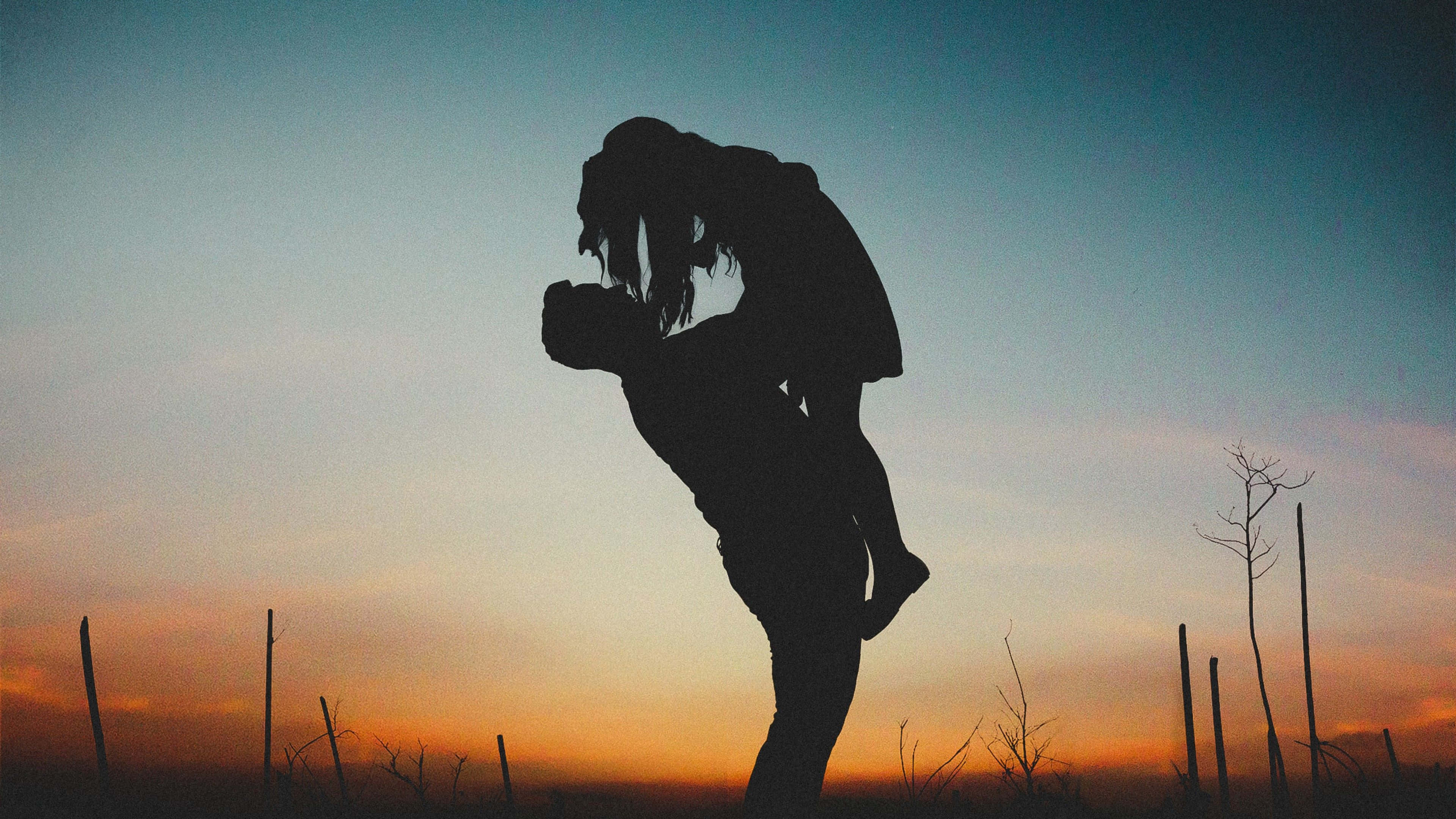 Silhouette 桌布 壁紙 — 剪影情侶在充滿活力的日落天空下，以裸樹和籬笆柱為背景，熱情擁抱。