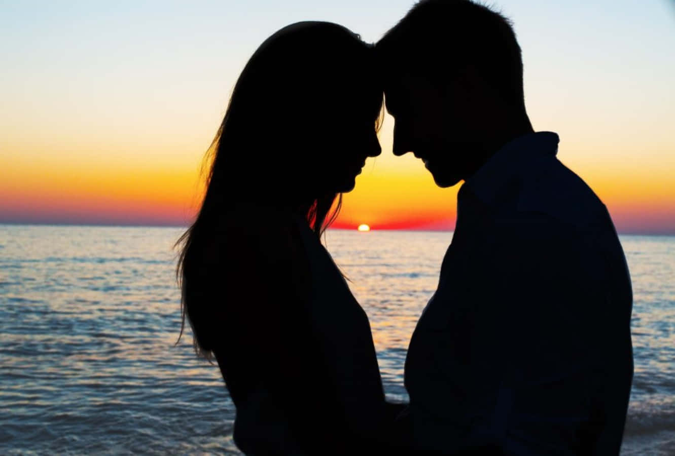 Falling In Love 桌布 壁紙 — 剪影情侶在平靜海平線上的日落中額頭相觸。