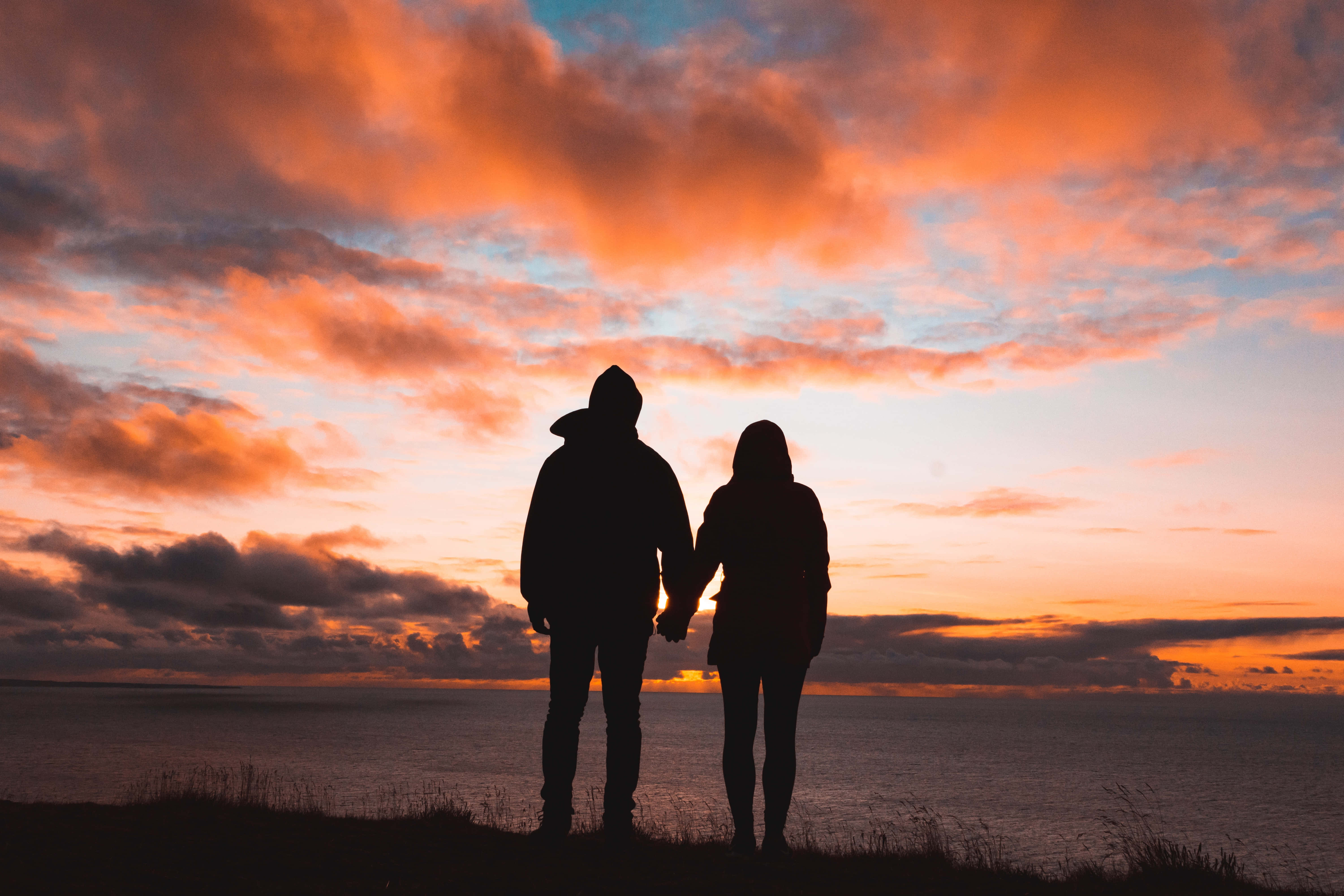 Love Couple 桌布 壁紙 — 剪影情侶在懸崖邊牽手，看著海洋地平線上熾熱的日落。