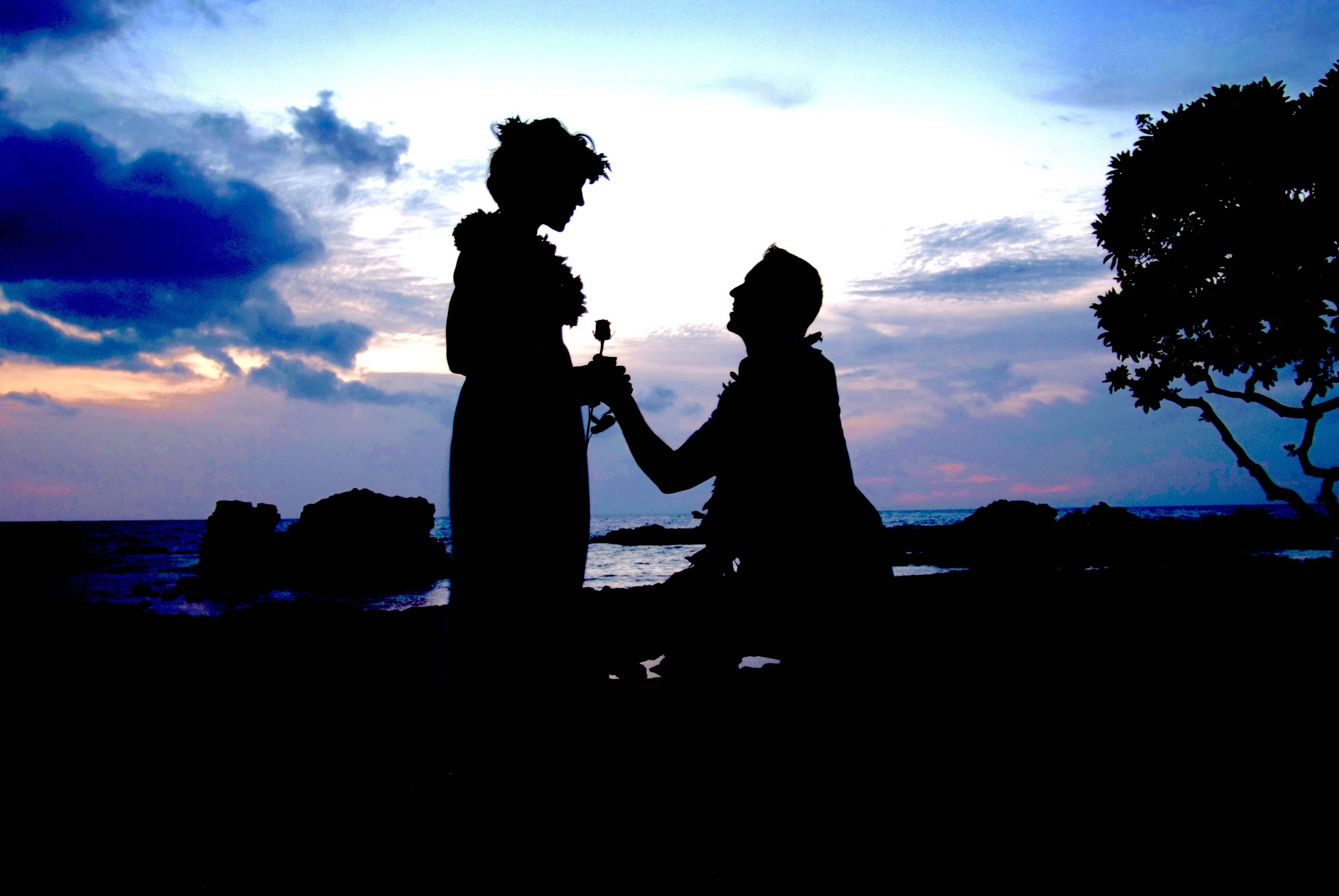 Romantic Love 桌布 壁紙 — 剪影情侶在日落時分於岩石海灘上分享溫馨時刻，背後有戲劇性的雲層和海洋。
