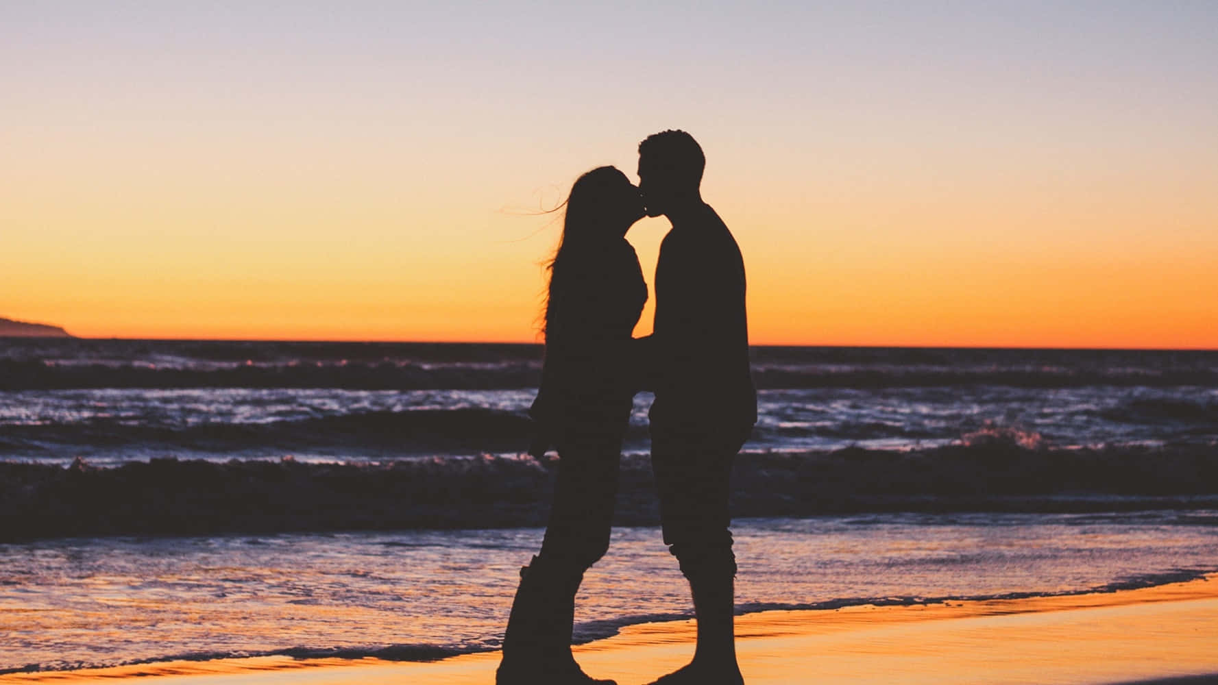 couple love 桌布 壁紙 — 剪影情侶在沙灘上親吻，夕陽橙色的天空和海洋波浪。