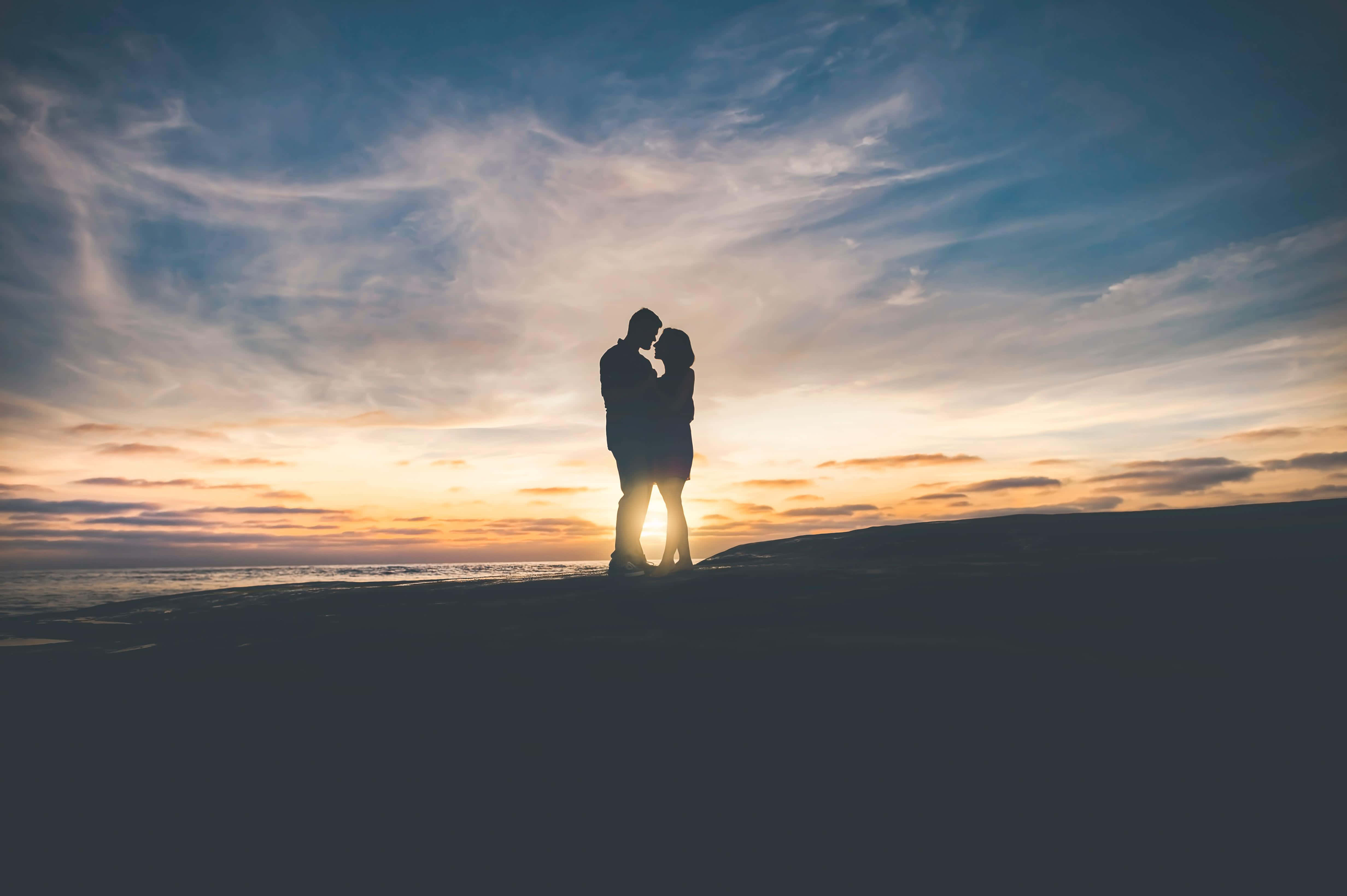 couple love 桌布 壁紙 — 剪影情侶在海灘上擁抱，金色夕陽光芒在他們身後映照著條紋天空。