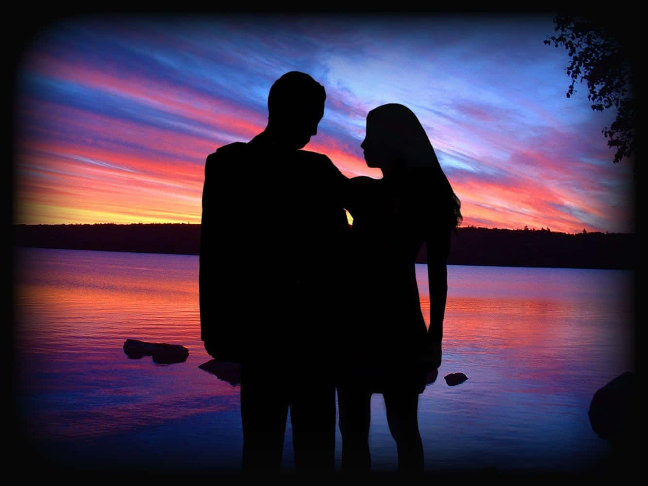couple love 桌布 壁紙 — 剪影情侶在湖邊擁抱，熾熱的夕陽將天空染成鮮豔的粉紅、紫色和橙色。