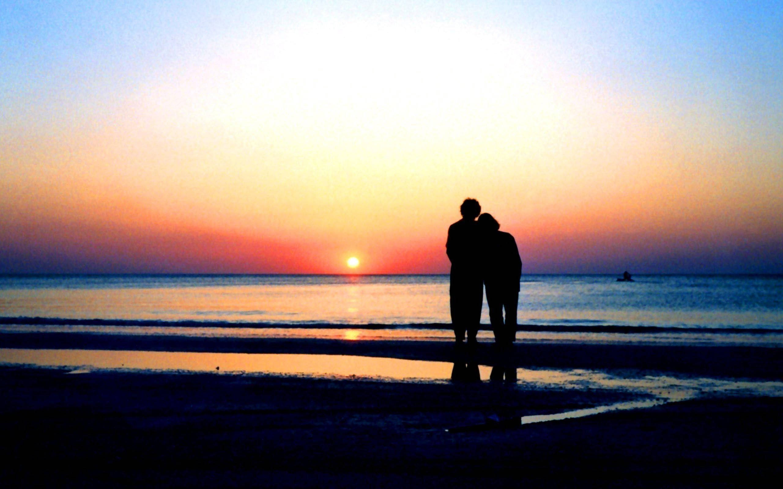 Silhouette 桌布 壁紙 — 剪影情侶在濕漉漉的海灘上擁抱，夕陽在平靜的海洋上落下，散發溫暖的光芒。