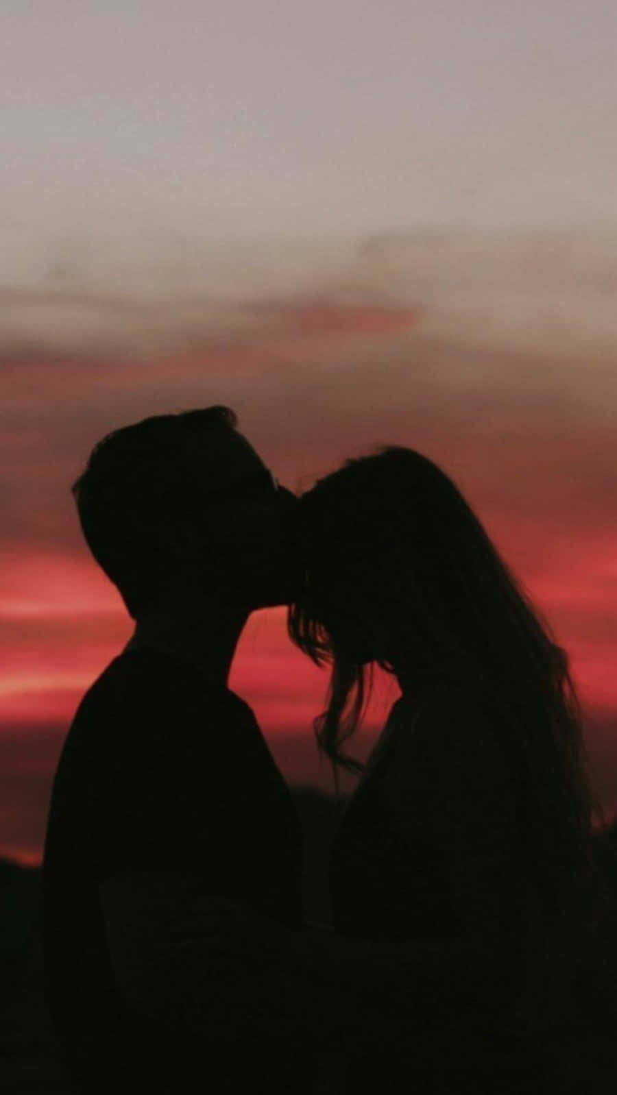 Aesthetic Couple 桌布 壁紙 — 剪影情侶在火紅的日落天空下親吻，帶有柔和粉紅和橙色色調。