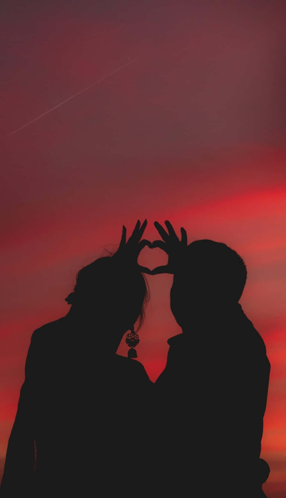 lover 桌布 壁紙 — 剪影情侶用雙手形成心形，背景是火紅的日落天空，帶有淡淡的飛機尾跡。