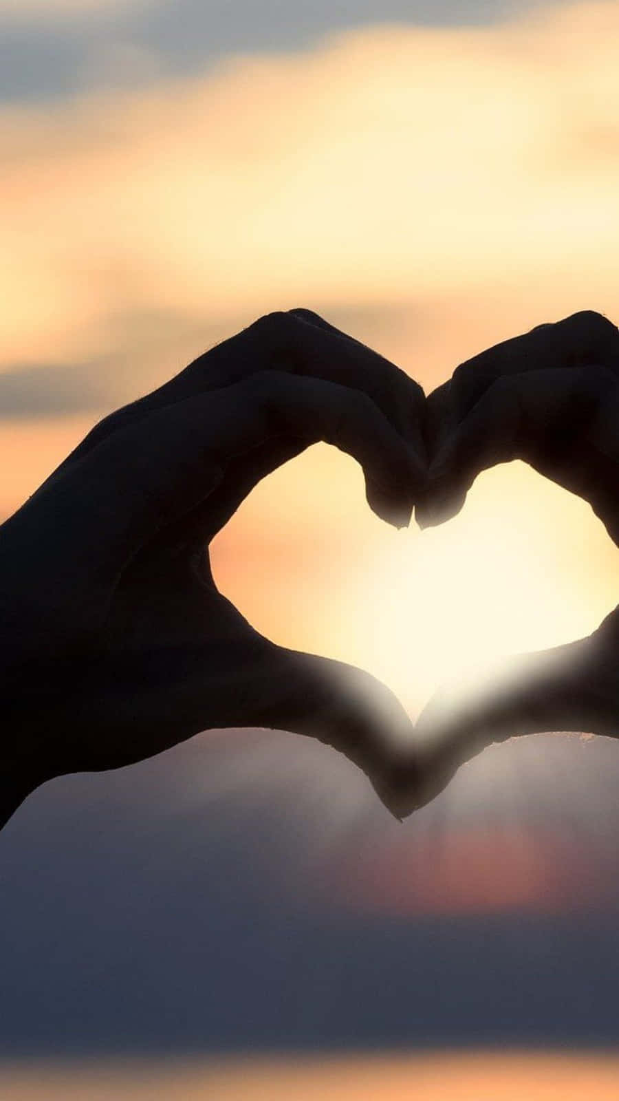 Heart Shape 桌布 壁紙 — 剪影手形形成一個心形，框住帶有柔和橙色和紫色色調的發光日落天空。