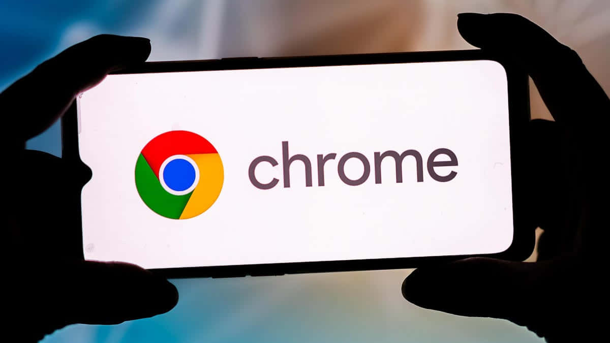 Chrome 桌布 壁紙 — 剪影手部拿著一支智慧型手機，在模糊的藍色背景上顯示色彩繽紛的 Chrome 標誌。
